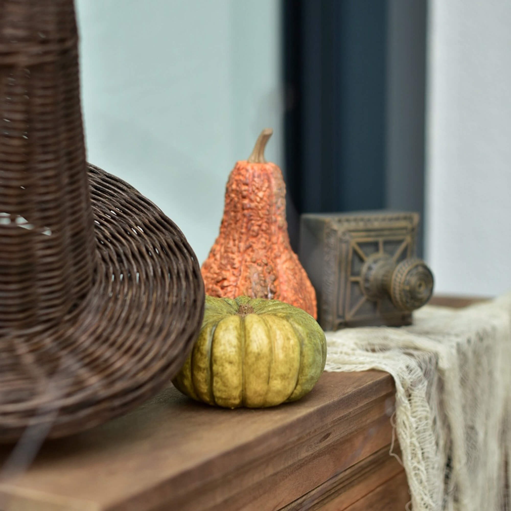 Dekorative grüne und orangefarbene Kürbisse auf Holzplatte neben einem Korb aus Weide