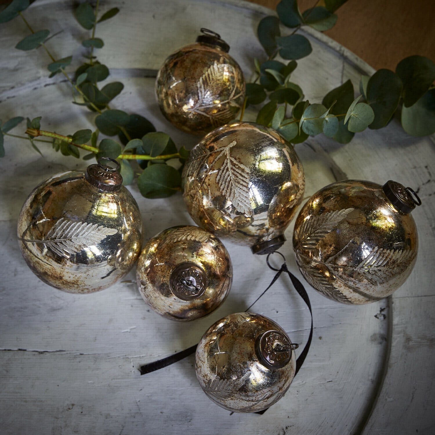Weihnachtsschmuck 6er Set Tristan Sechs goldene Glas-Weihnachtskugeln mit Blattmotiv auf weißem Tablett mit grünen Zweigen