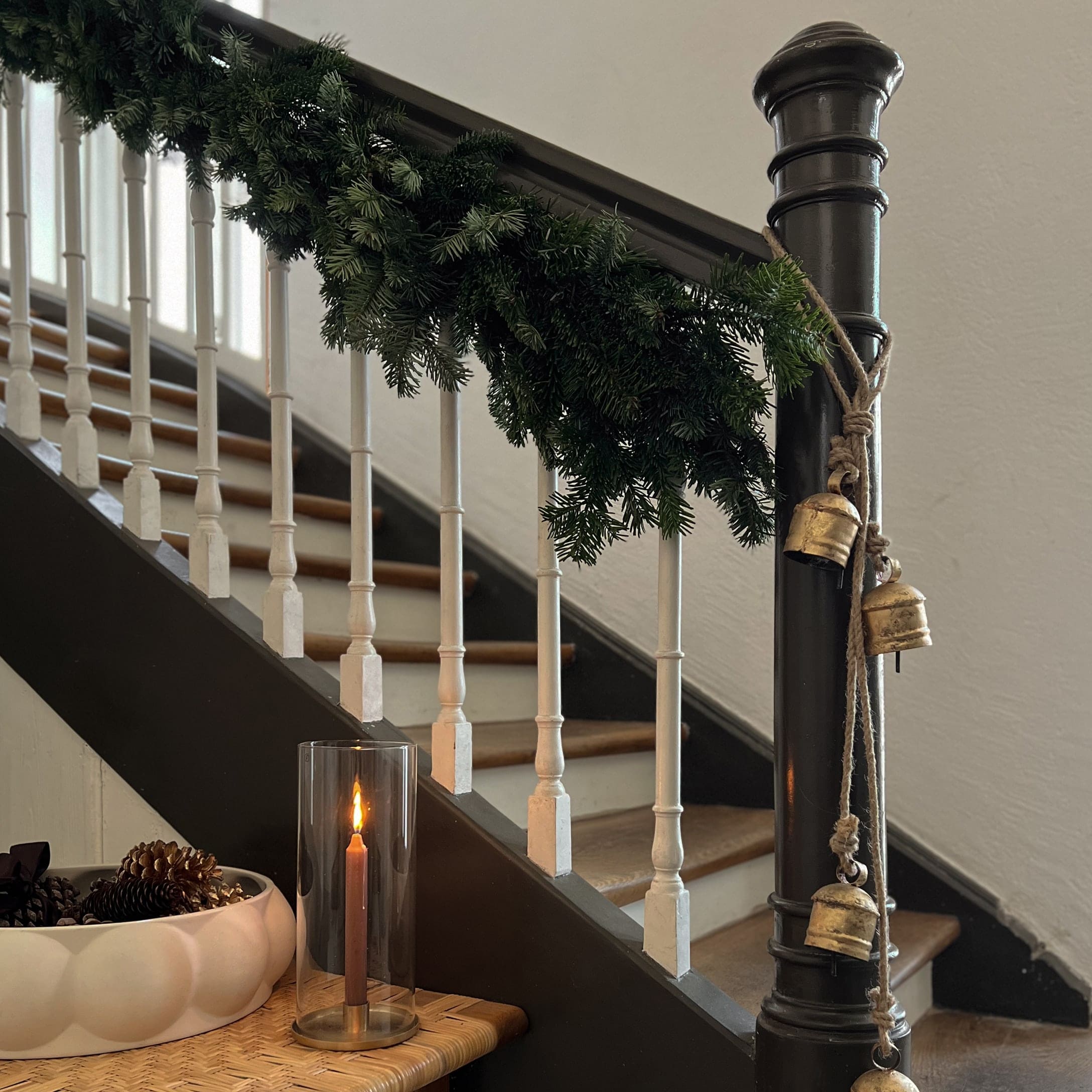 Treppendekoration mit grünem Tannengirlande, goldenen Glocken und brennender Kerze im Glaswindlicht auf Holztisch