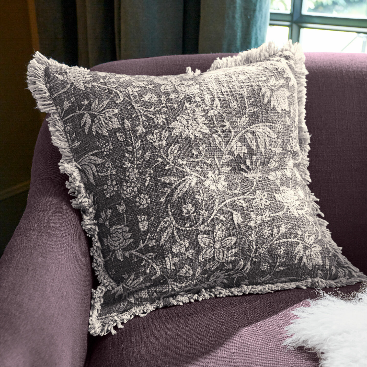 Kissenhülle Jorelise Graues Dekokissen mit weißem Blumenmuster und Fransen auf violettem Sofa