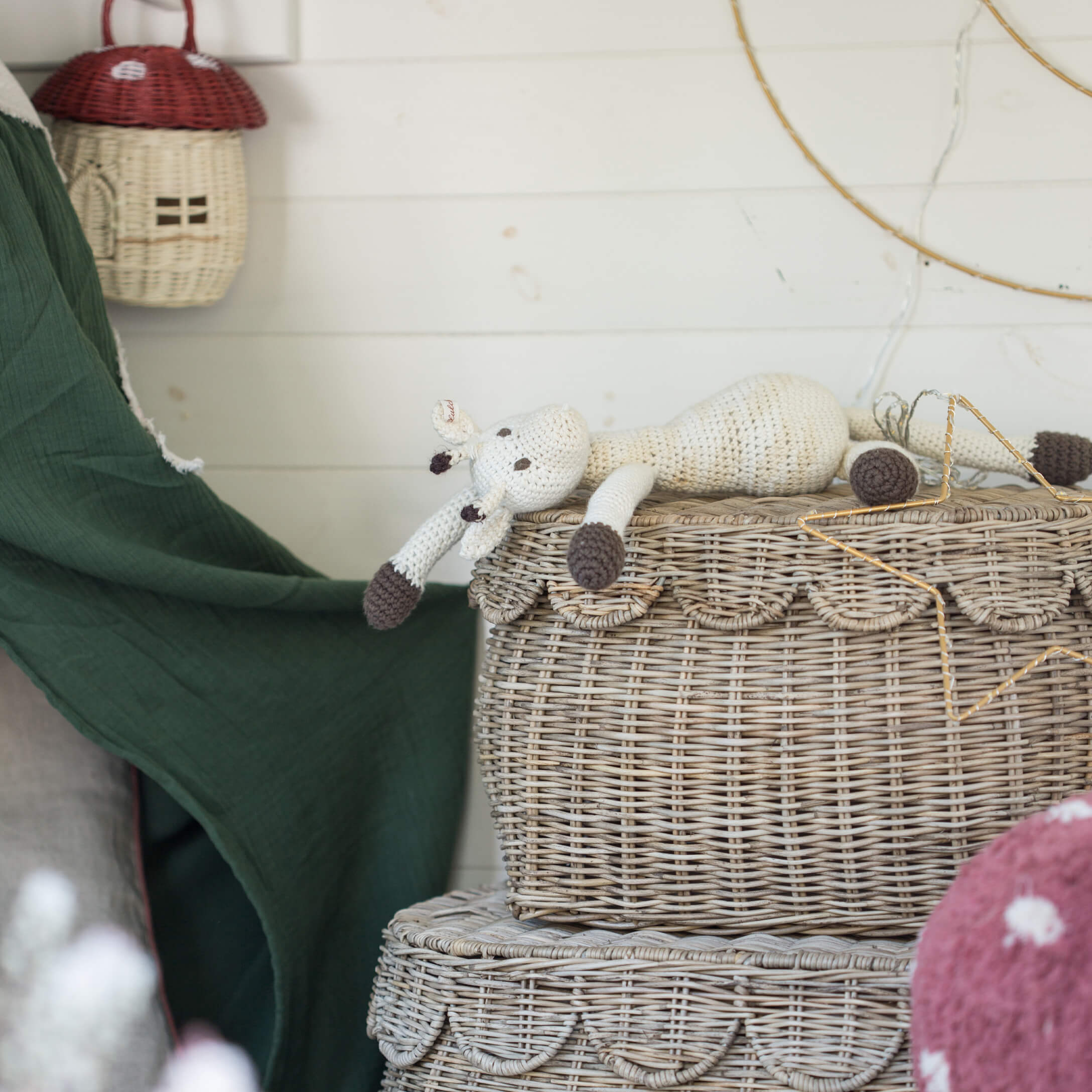 Handgehäkelte weiße und braune Giraffenpuppe auf einem dekorativen Korb aus Rattan im Boho-Stil