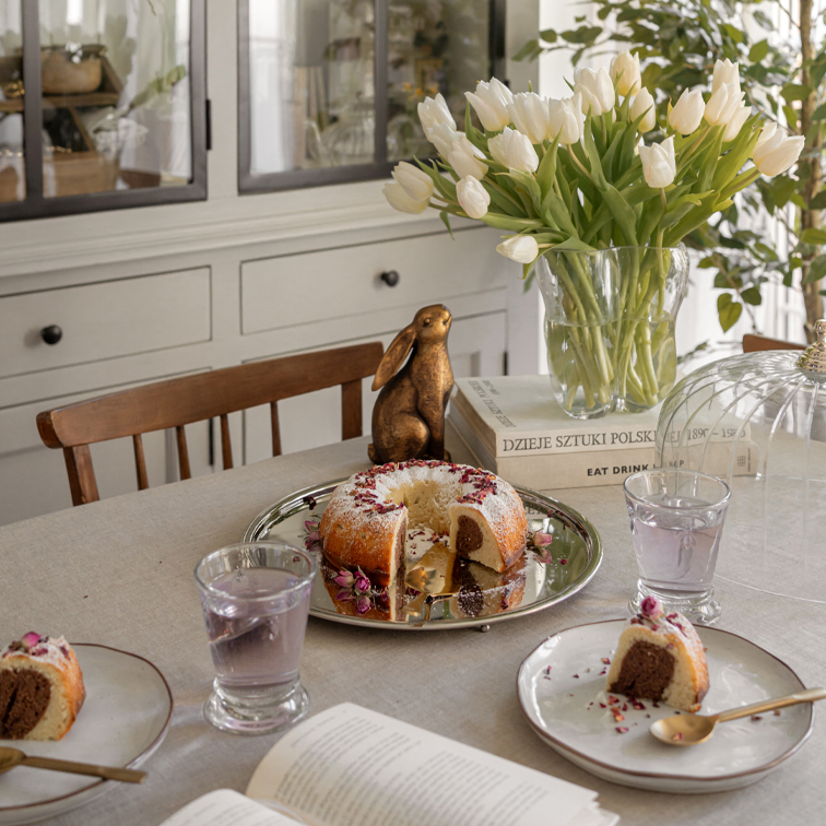 Tisch mit Marmorkuchen auf silbernem Tablett, weißen Tulpen in Glasvase und dekorativem Hasen