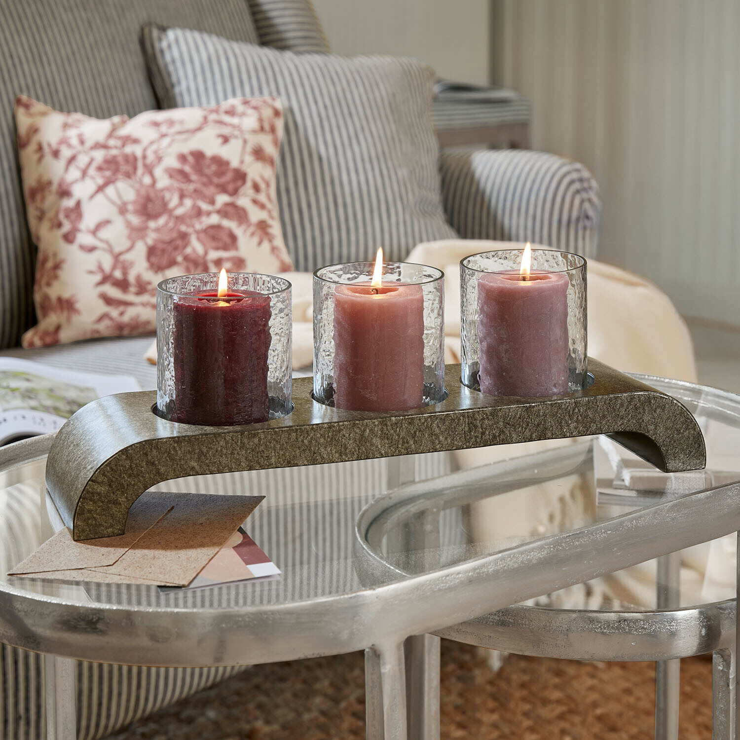 Drei brennende Kerzen in Gläsern auf einem Metallständer auf einem Glastisch im Wohnzimmer