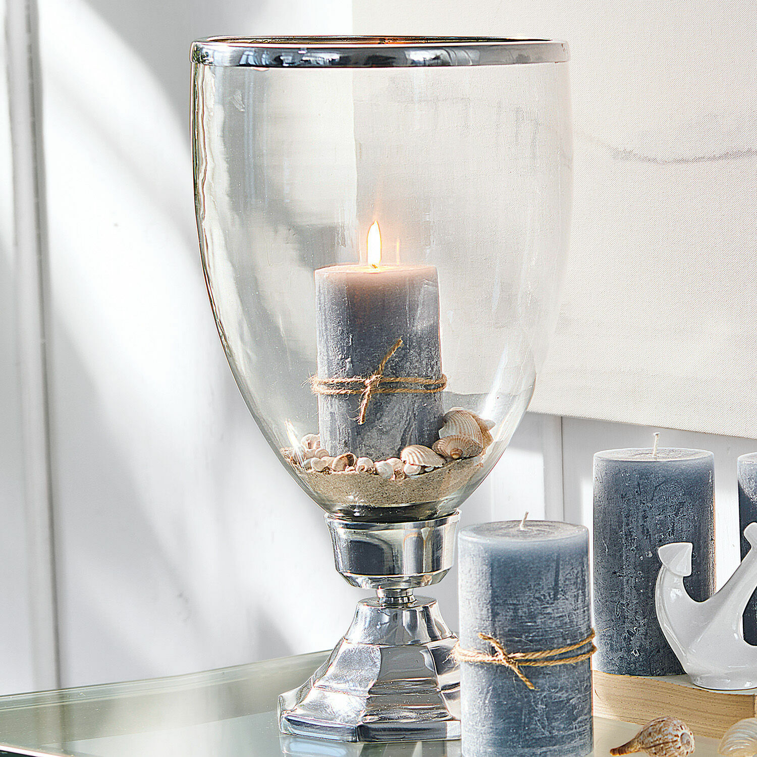 Kerzenständer Echelon Graue Kerze mit Juteschnur in Glaswindlicht mit Muscheln und Sand auf Tisch