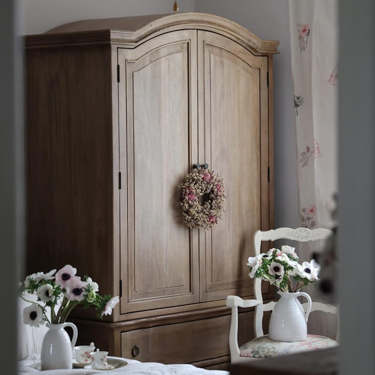 Holzschrank mit dekorativem Kranz und weißem Stuhl mit Blumen in Vase, rustikaler Stil