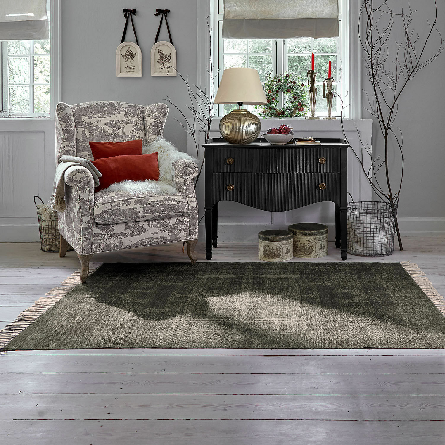 Gemütlicher Sessel mit beige-grauem Muster und roten Kissen neben schwarzer Vintage-Kommode im Wohnzimmer