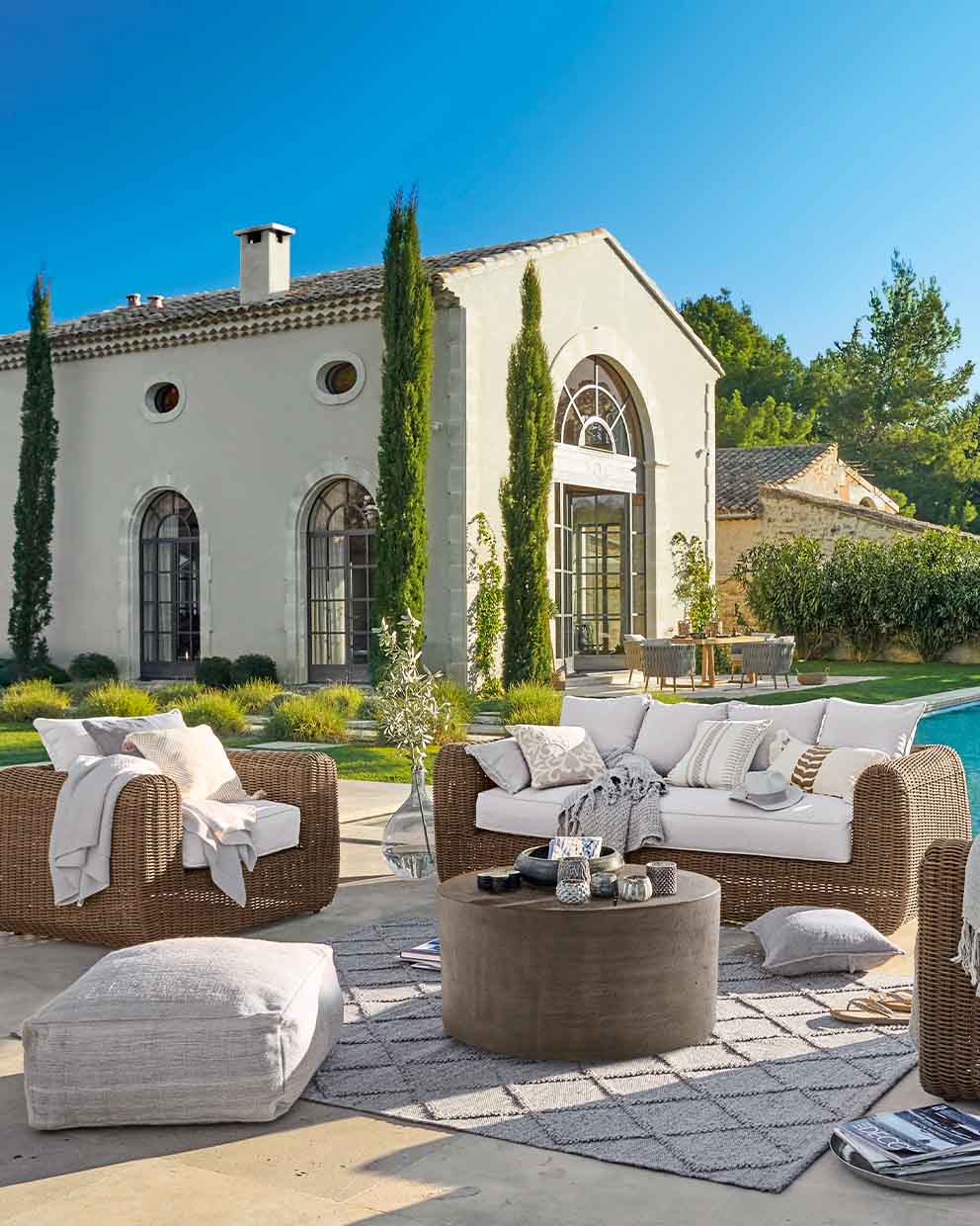 Braunes Rattan-Gartenmöbel-Set mit weißen Kissen auf Terrasse neben Pool bei sonnigem Wetter
