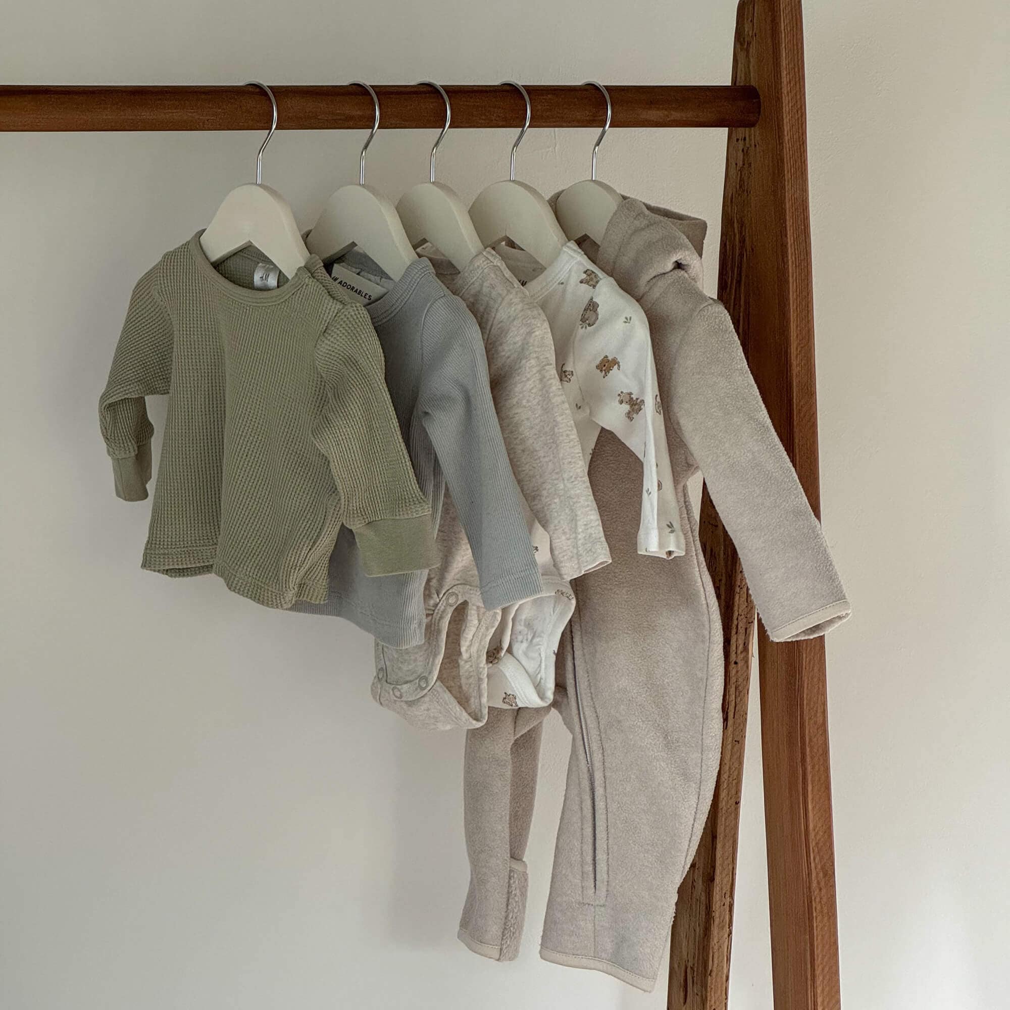 Set aus Babybekleidung in neutralen Farben an Kleiderbügeln, weiche Stoffe mit Bärenmotiven
