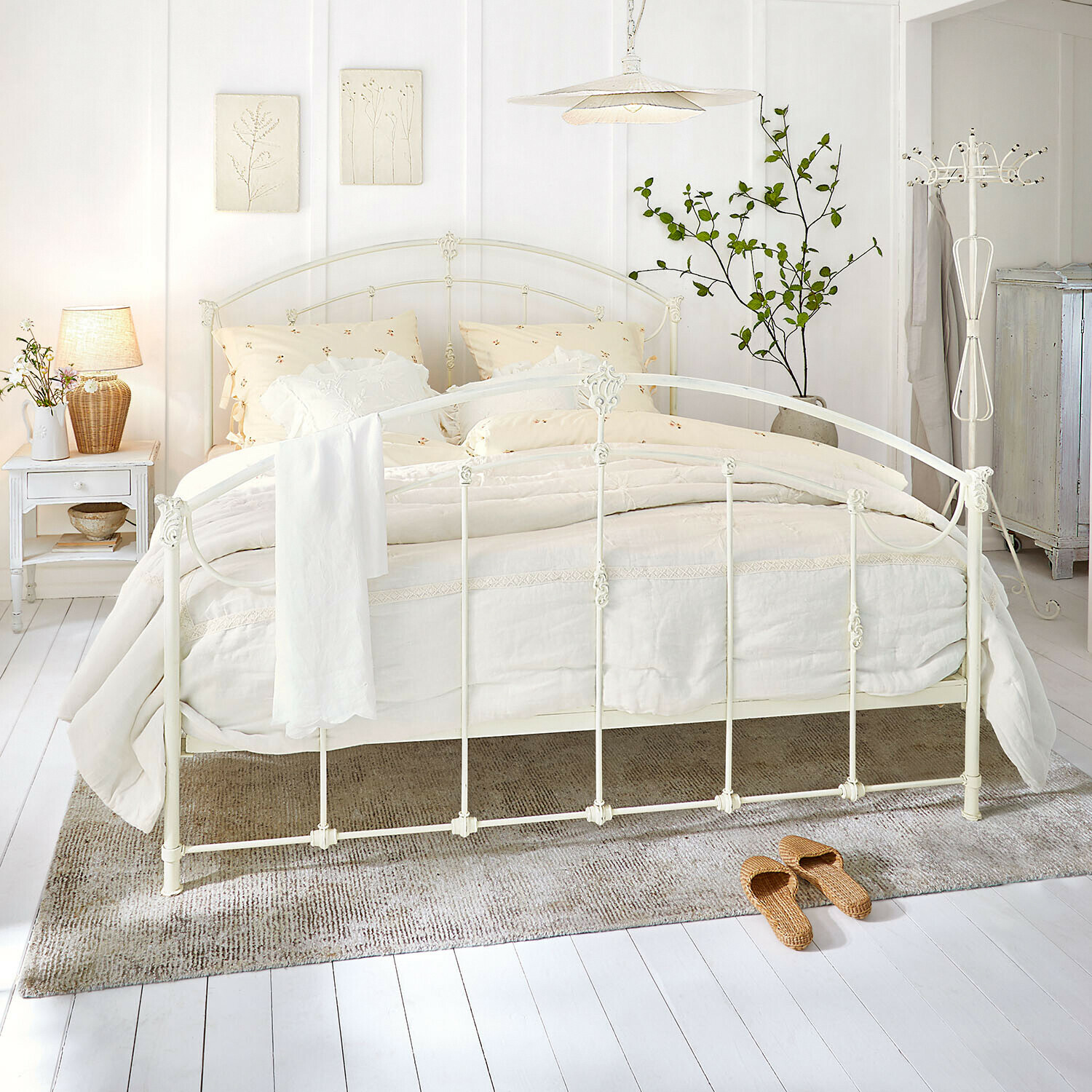 Weißes Metallbett mit cremefarbener Bettwäsche und Naturteppich in hellem Schlafzimmer