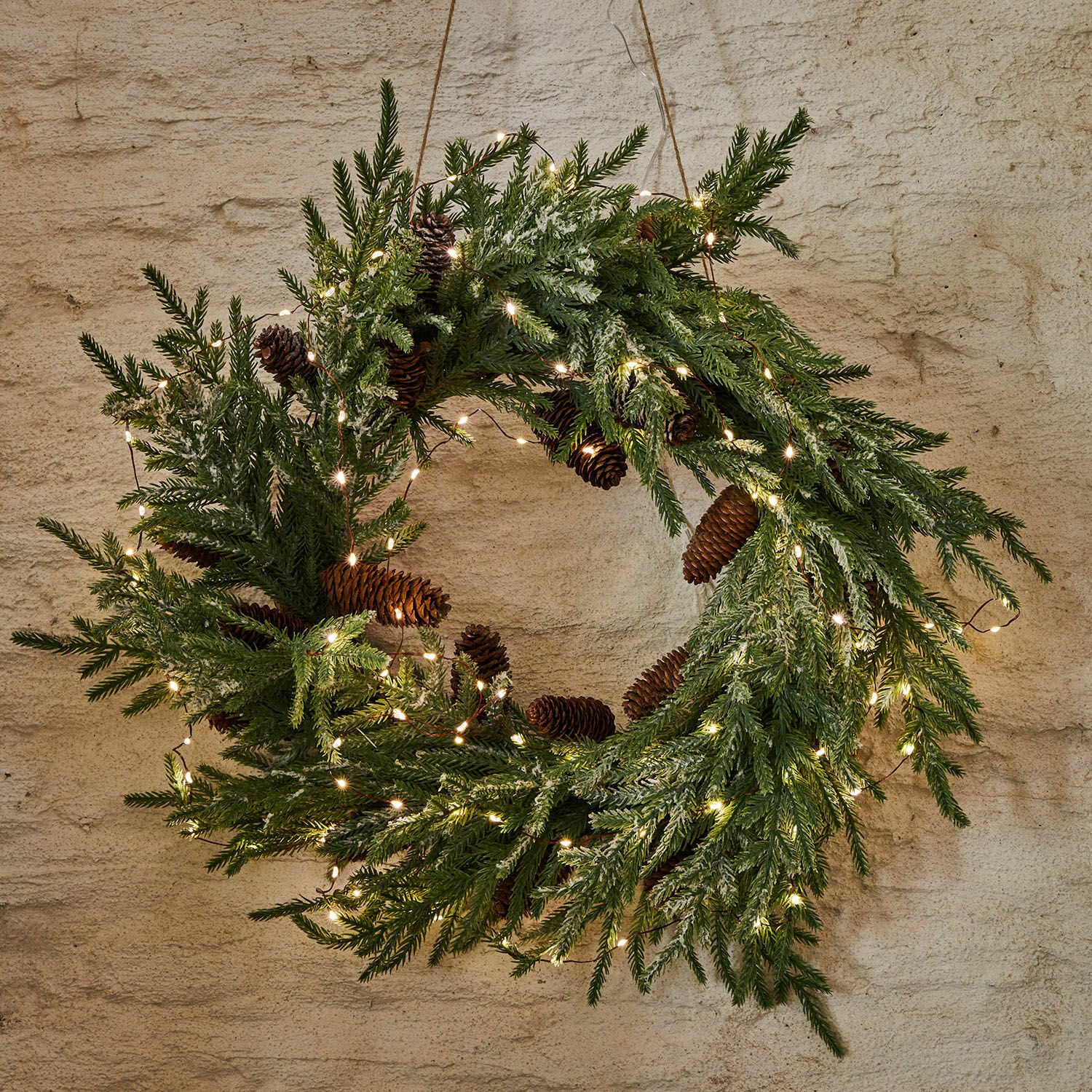 Weihnachtskranz aus grünen Zweigen und Zapfen mit LED-Lichterkette an der Wand hängend