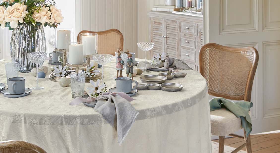 Zart dekorierter Ostertisch mit cremefarbenem Tischdecke, Kerzen und feinem Porzellan-Geschirr