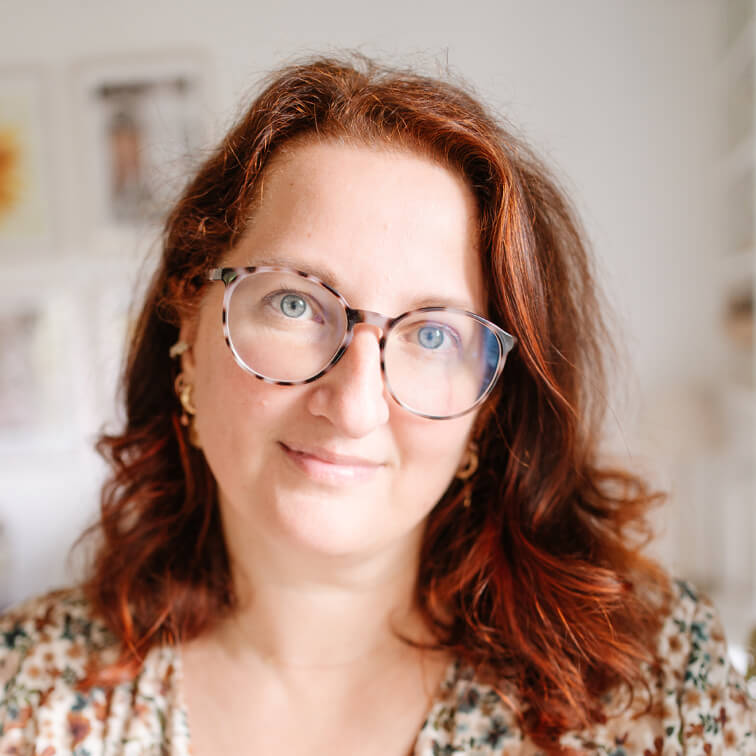 Porträt einer Frau mit roten Haaren und Brille in hellem, unscharfem Innenraum