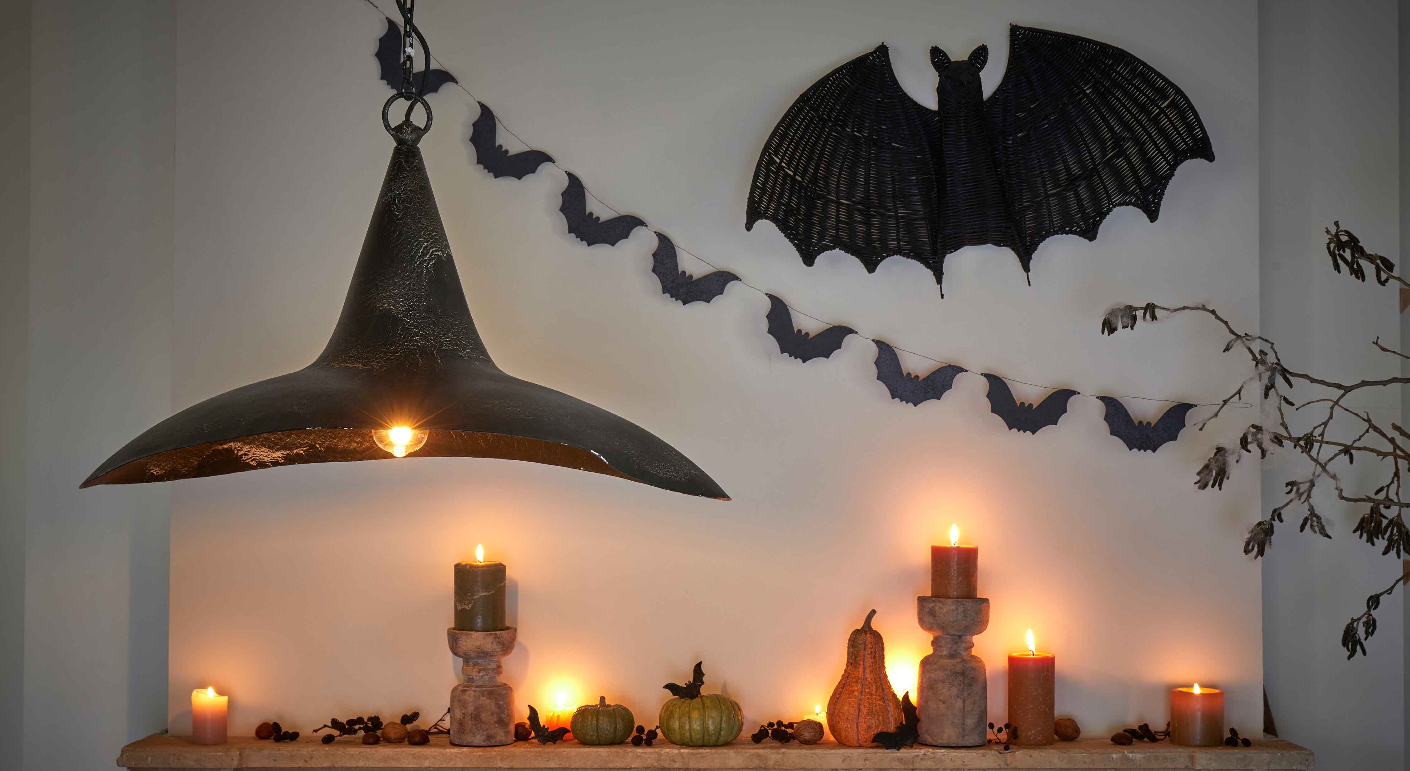 Halloween-Dekoration mit schwarzen Kerzen, Kürbissen und schwarzer Metalllampe an Wand mit Fledermäusen