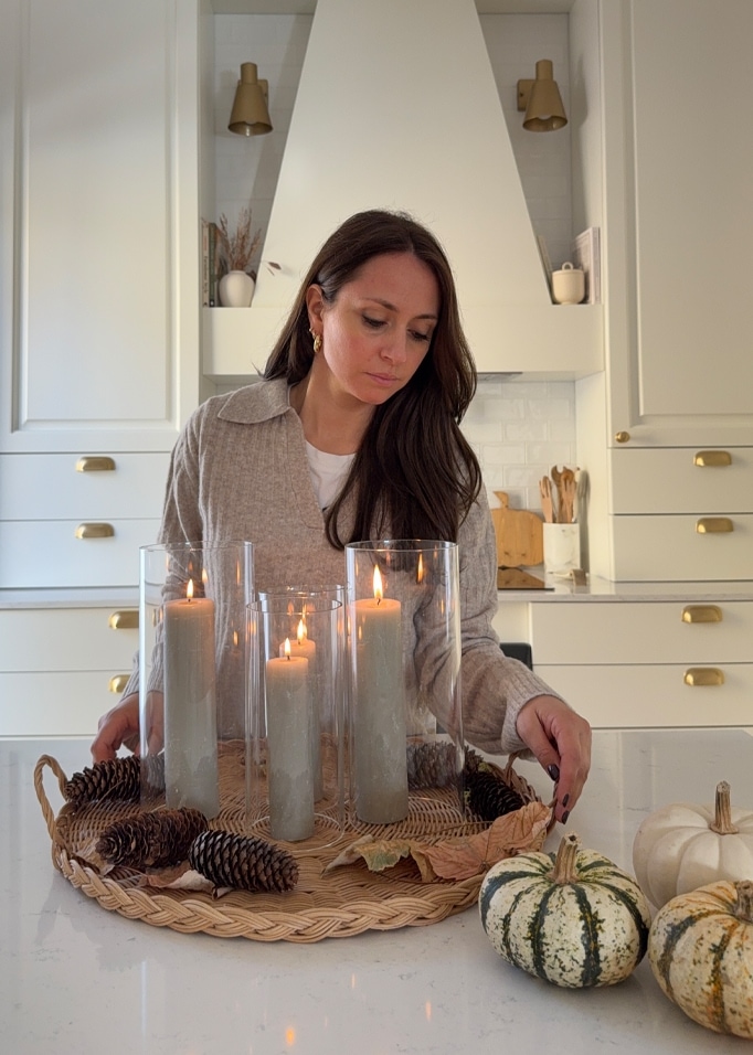 Frau mit herbstlichem Dekotablett mit grauen Kerzen, Kiefernzapfen und Kürbissen in der Küche