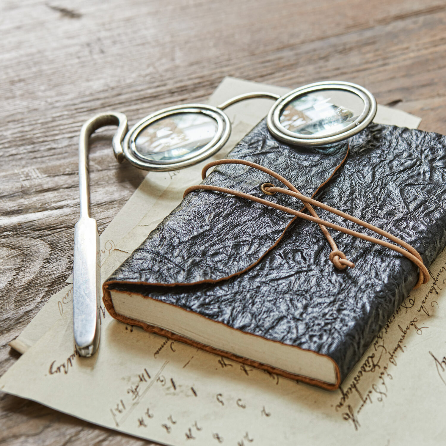 Lupe Robert Schwarzes Notizbuch aus weichem Leder mit Schnurverschluss auf Holztisch mit Brille und alten Briefen