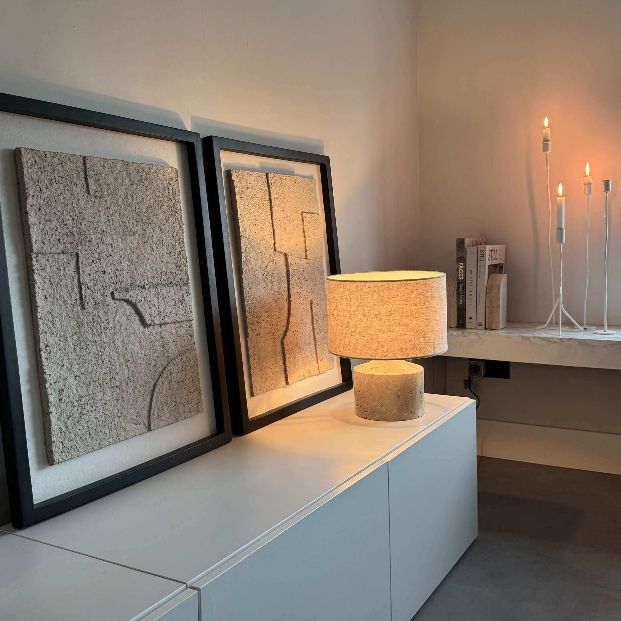 Moderne Tischlampe mit beigem Stoffschirm und Steinsockel auf weißem Sideboard mit Wanddekoration