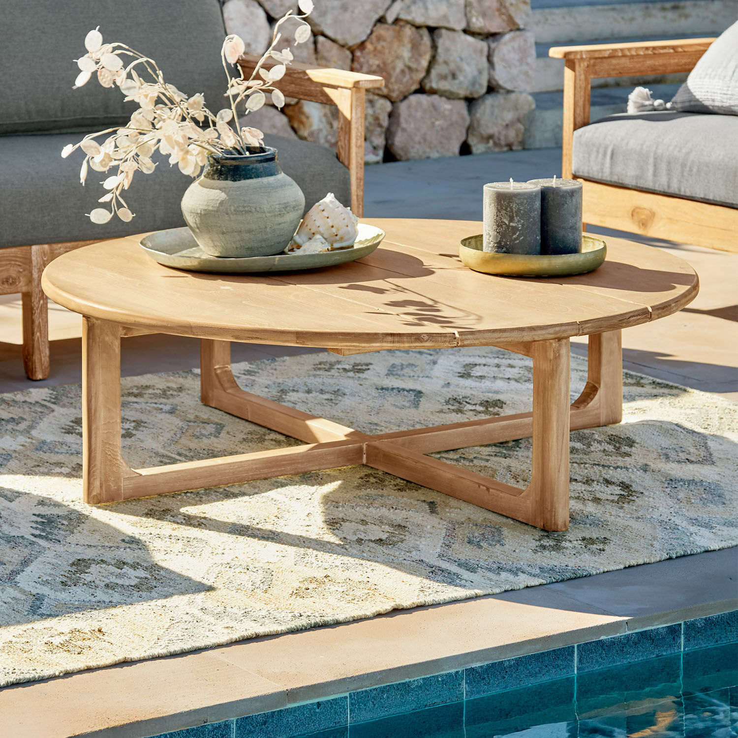 Couchtisch Tewksbury Runder Couchtisch aus naturfarbenem Teakholz auf Terrasse am Pool mit Dekorationen
