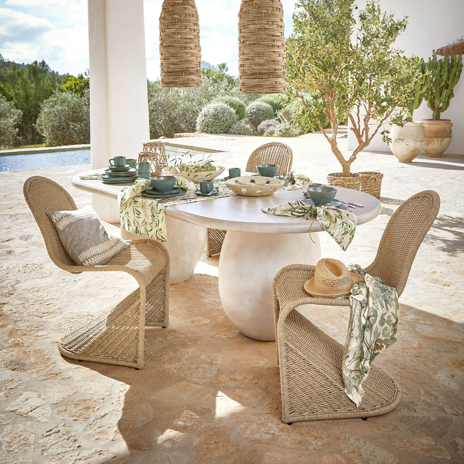 Tisch Arevalon Ovaler Tisch mit weißer Tischplatte und naturfarbenen Korbstühlen auf Terrasse mit Gartenblick