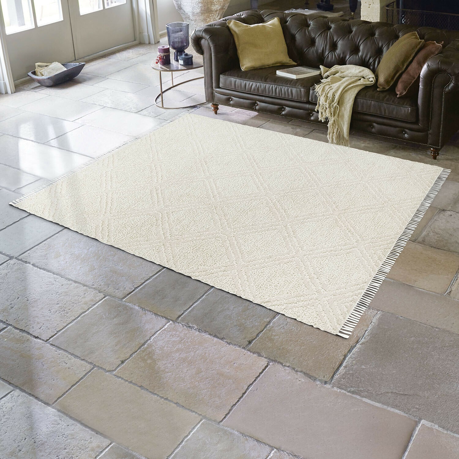 In- & Outdoor-Teppich Bruand Beigefarbener Teppich mit geometrischem Muster auf Steinboden im Wohnzimmer mit dunkelbraunem Ledersofa