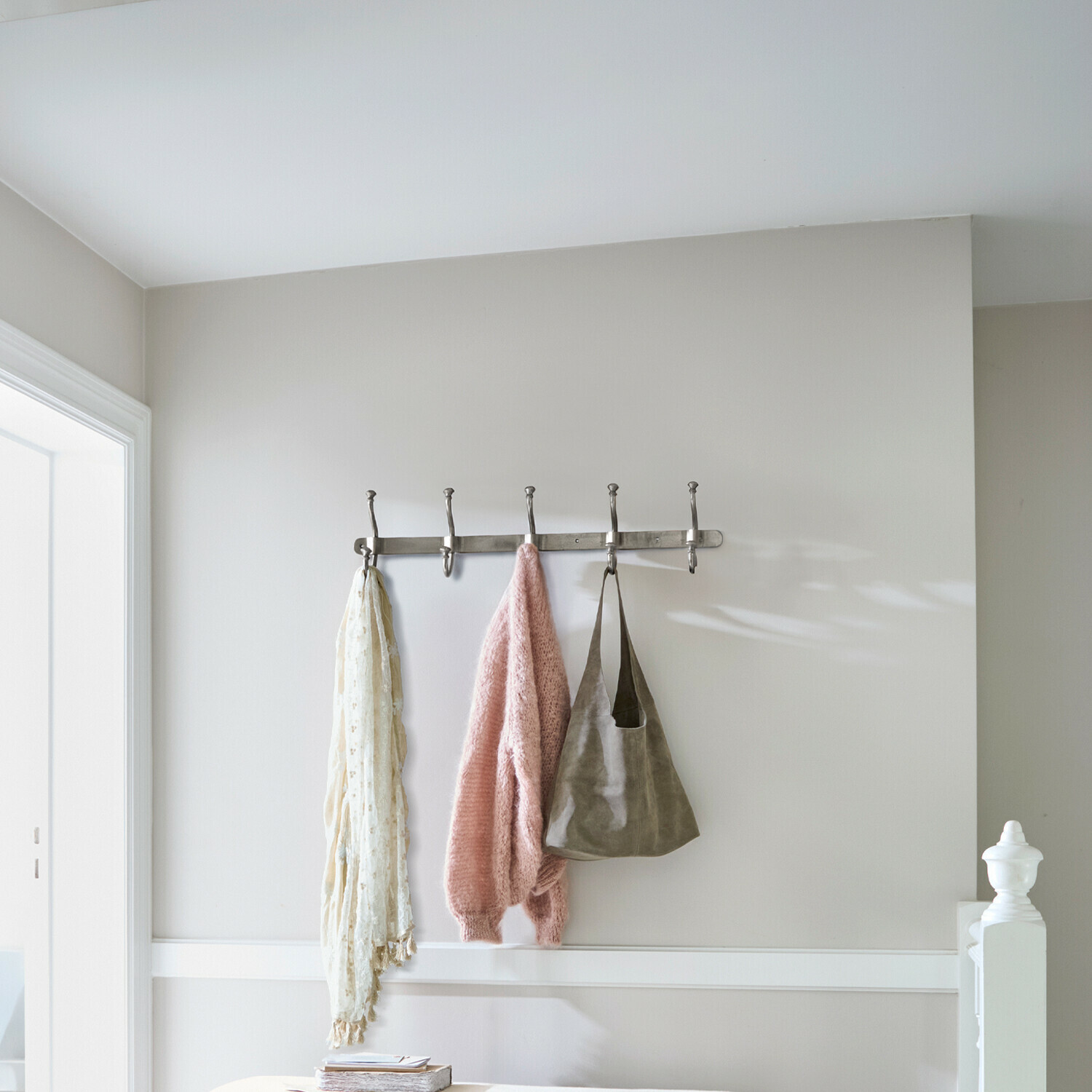 Metall-Wandgarderobe mit fünf Haken, daran hängen rosa Pullover, Schal und Tasche