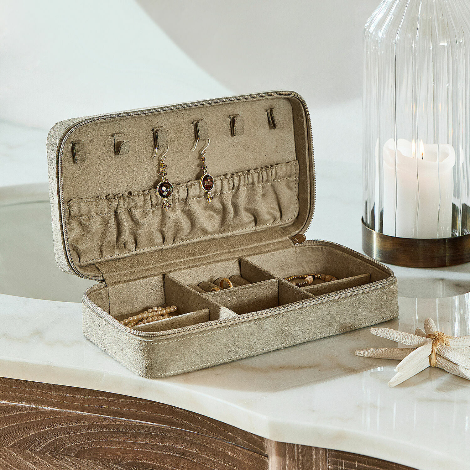 Beige Schmucketui aus Wildleder mit Fächern und Ohrringhaken auf Marmorplatte