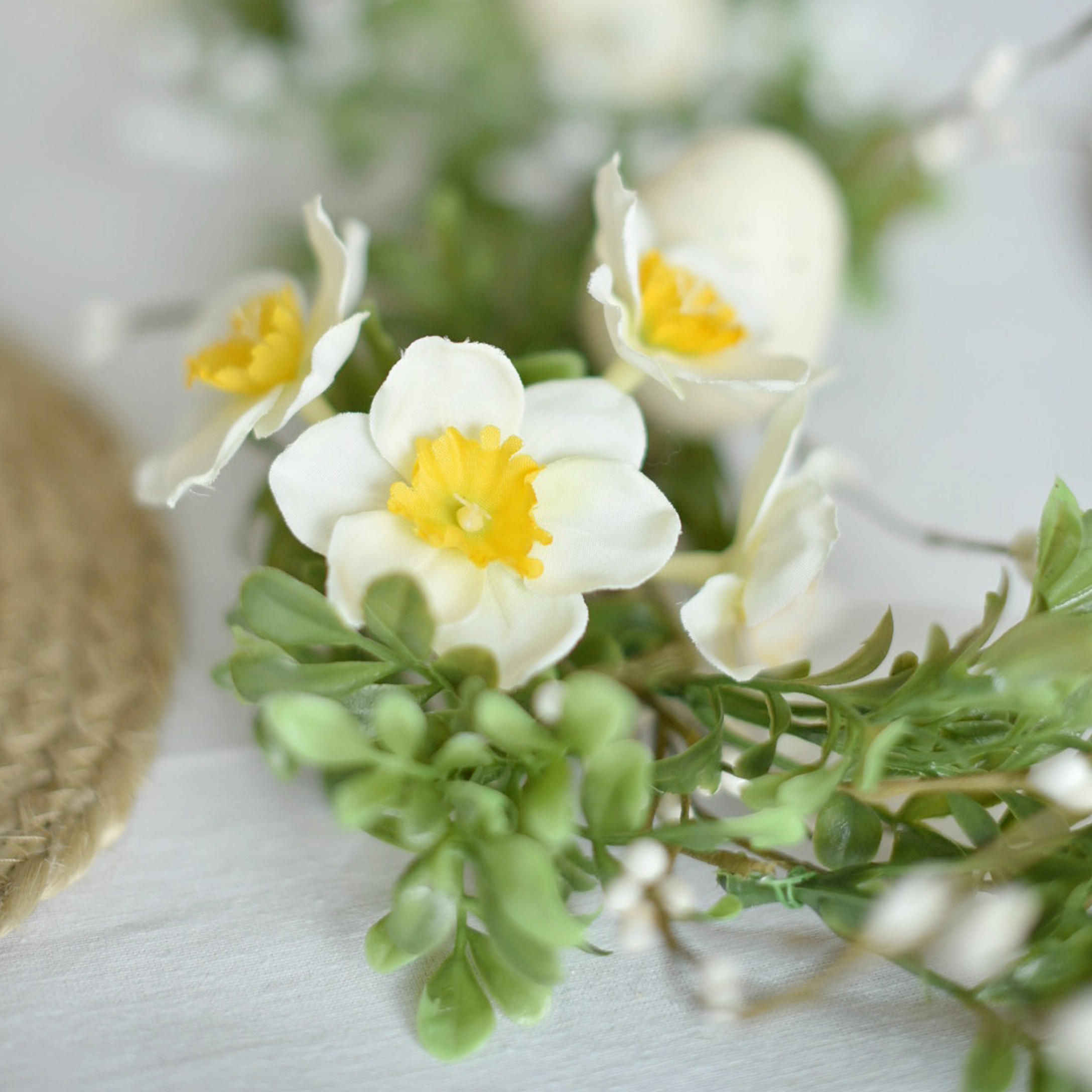 Dekorativer Kranz mit weißen und gelben Blüten sowie grünen Blättern auf hellem Hintergrund