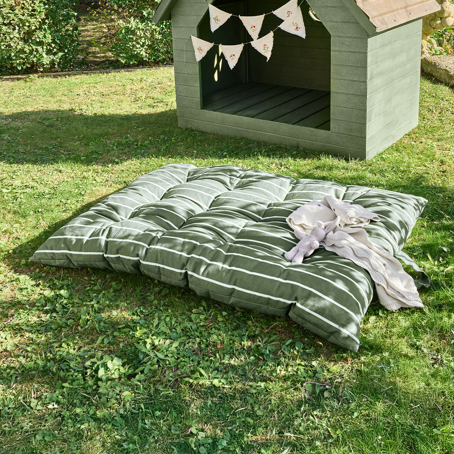 Weiche grün gestreifte Bodenkissen auf Gras neben einer Hundehütte aus Holz mit dekorativer Wimpelkette