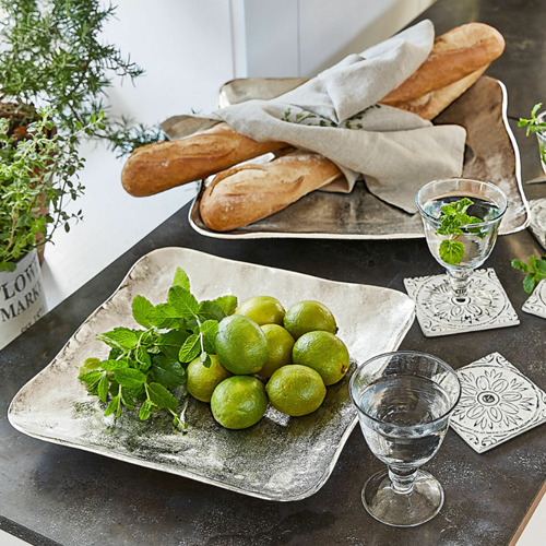 Quadratische silberne Metallplatte mit Limetten und Minze auf Tisch mit Baguette und Wassergläsern