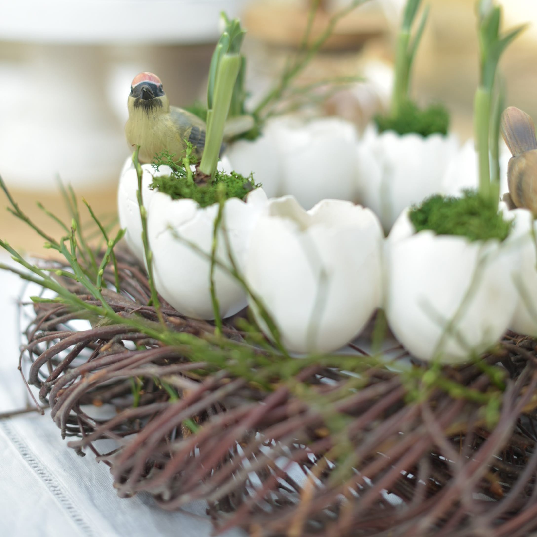 Dekorativer Kranz mit weißen Keramikeiern, grünem Moos und Vogel-Figuren für Osterdeko