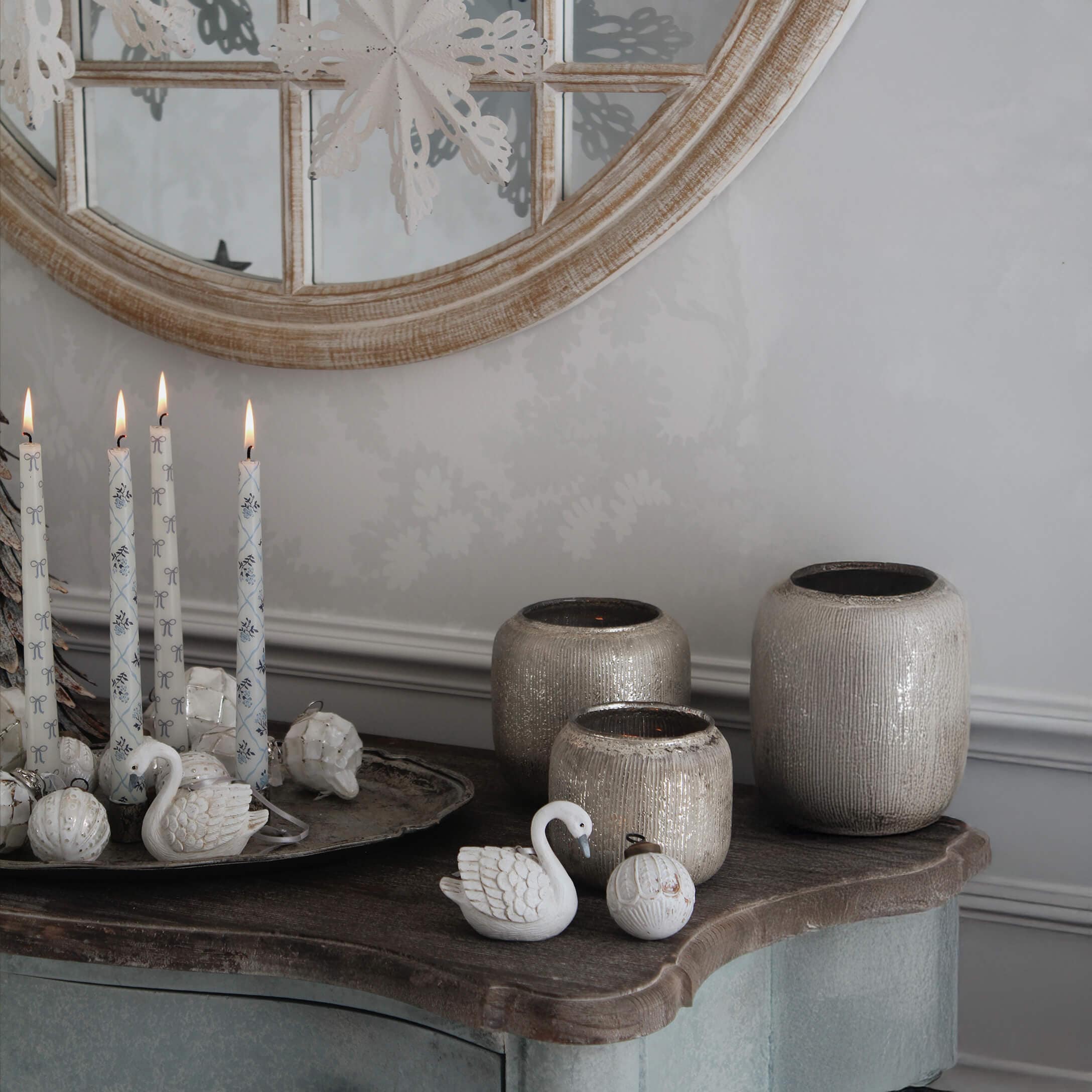 Dekorative weiße Kerzen und beige Keramikvasen auf Holzplatte vor rundem Spiegel