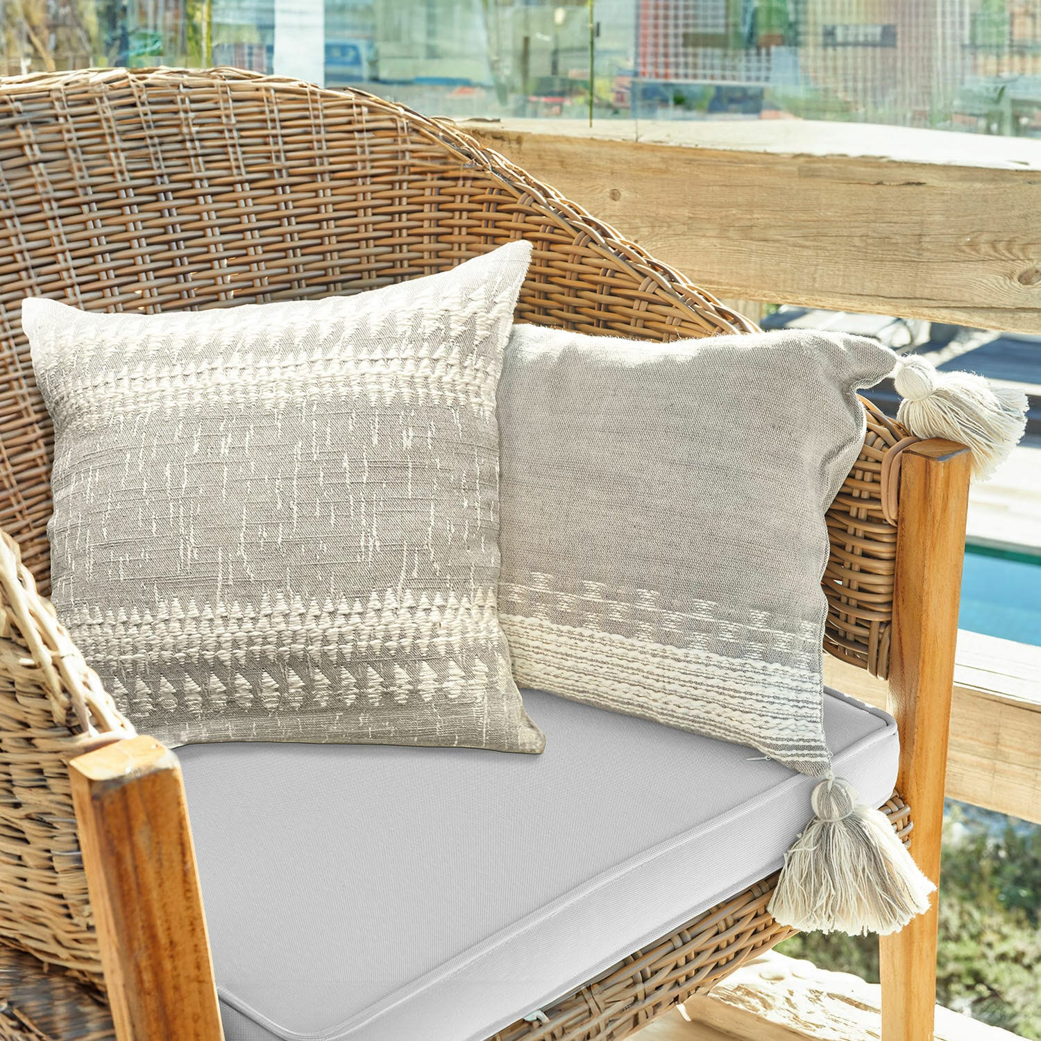 Kissenhülle 2er Set Fontavon Zwei beige Baumwoll-Dekokissen mit Quasten auf einem Rattansessel auf sonniger Terrasse