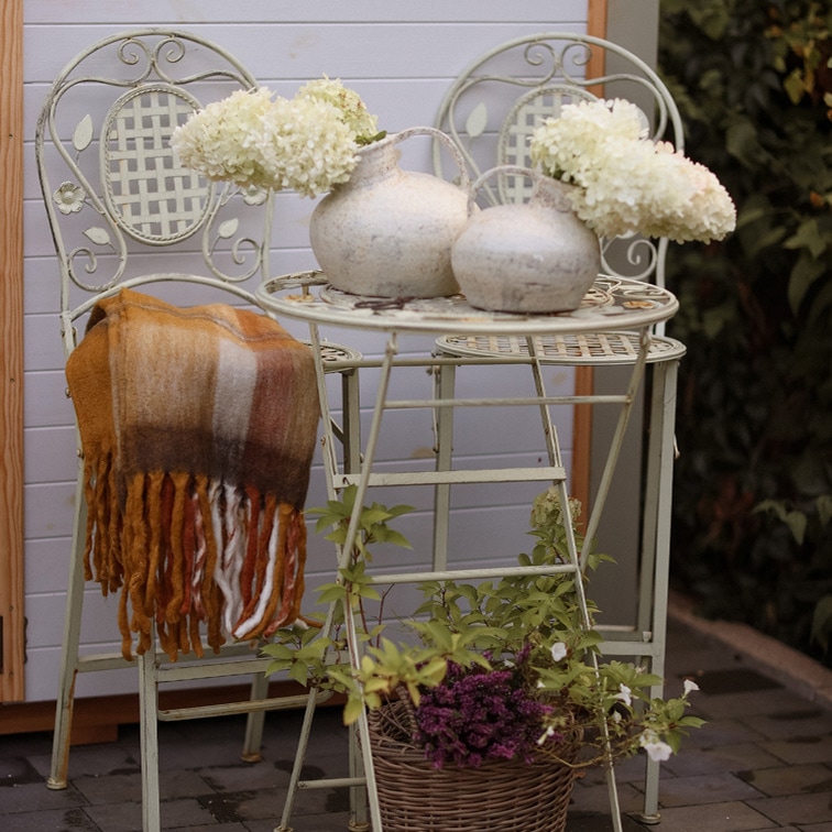 Heller Metalltisch und zwei Vintage-Stühle mit dekorativen weißen Vasen und Blumen im Garten