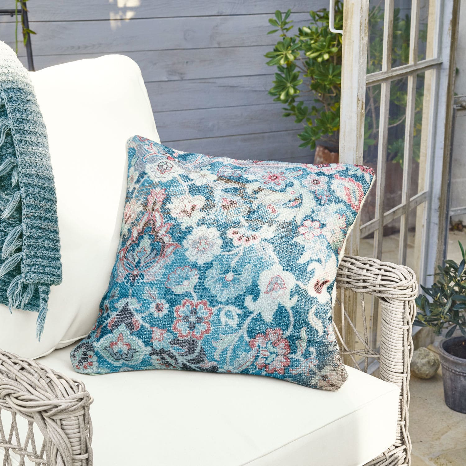 In- & Outdoor-Kissenhülle Obair Dekoratives Kissen aus Stoff mit blau-rosa Blumenmuster auf weißem Rattansessel