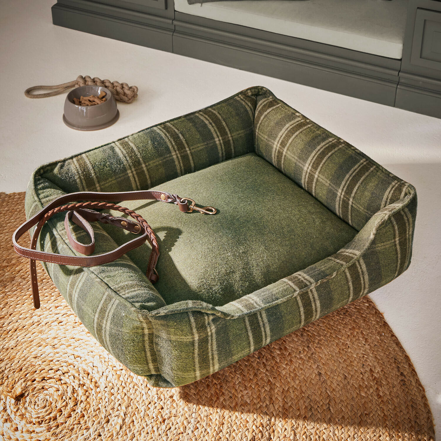 Grünes Hundebett aus weichem kariertem Stoff mit braunem Lederleine und Futternapf mit Leckerlis