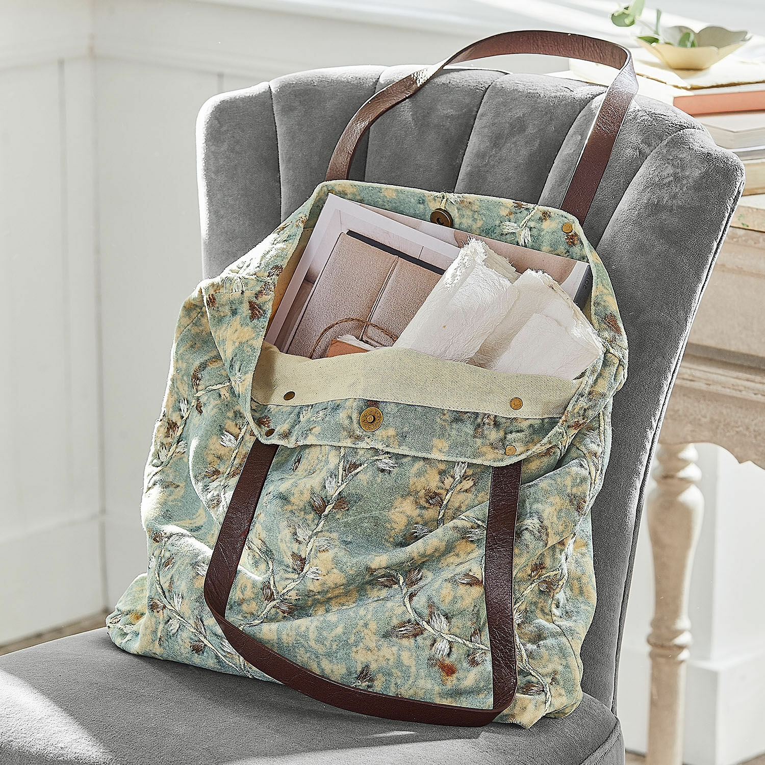 Tasche LaRoux Tasche aus weichem Stoff in grün-beigem Muster mit braunen Griffen auf grauem Stuhl