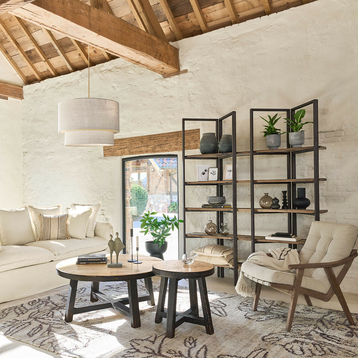 Gemütliches Wohnzimmer mit Holztischen, cremefarbenem Sofa und Metallregal mit Dekorationen