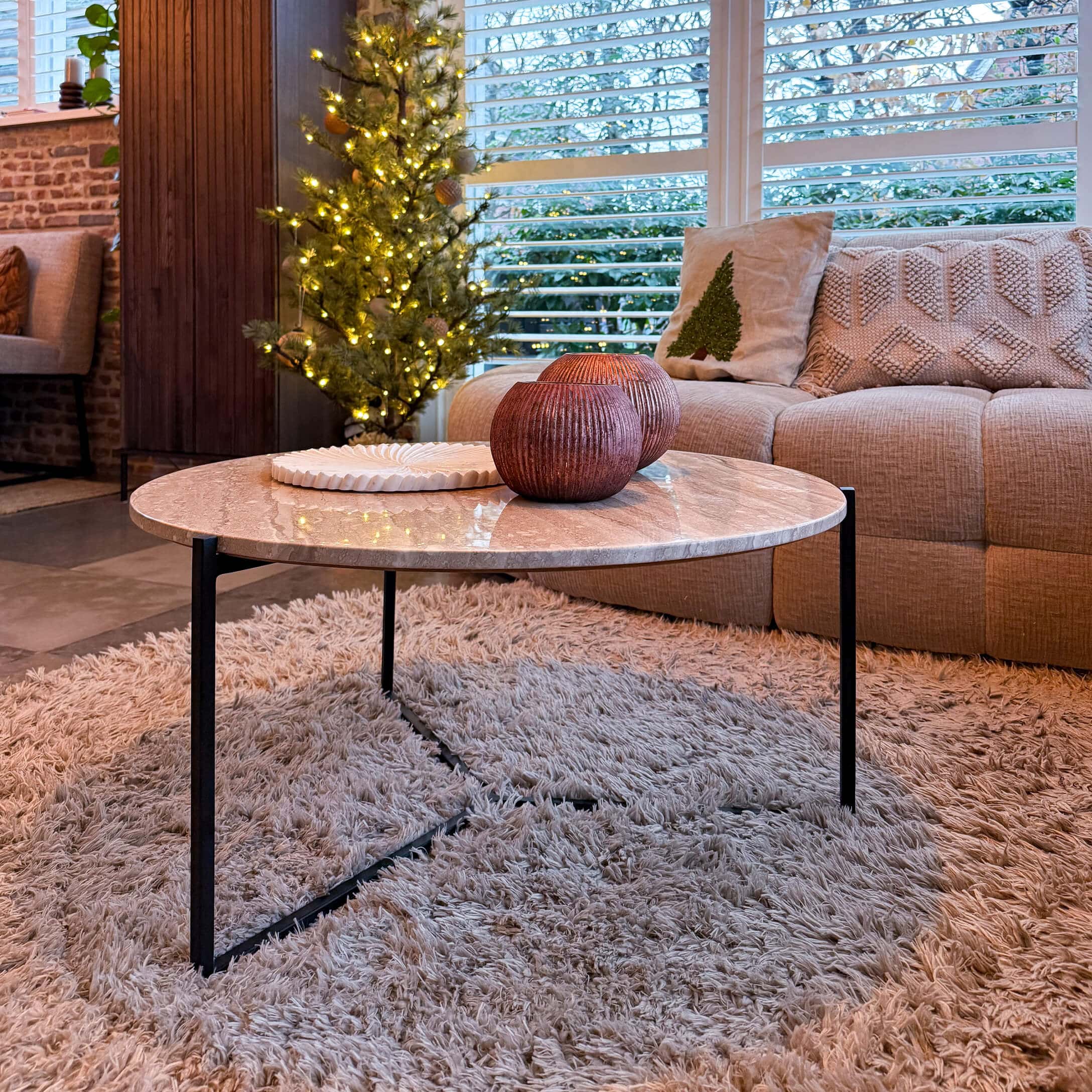 Runder Couchtisch mit Marmorplatte und schwarzem Metallgestell auf flauschigem Teppich im Wohnzimmer