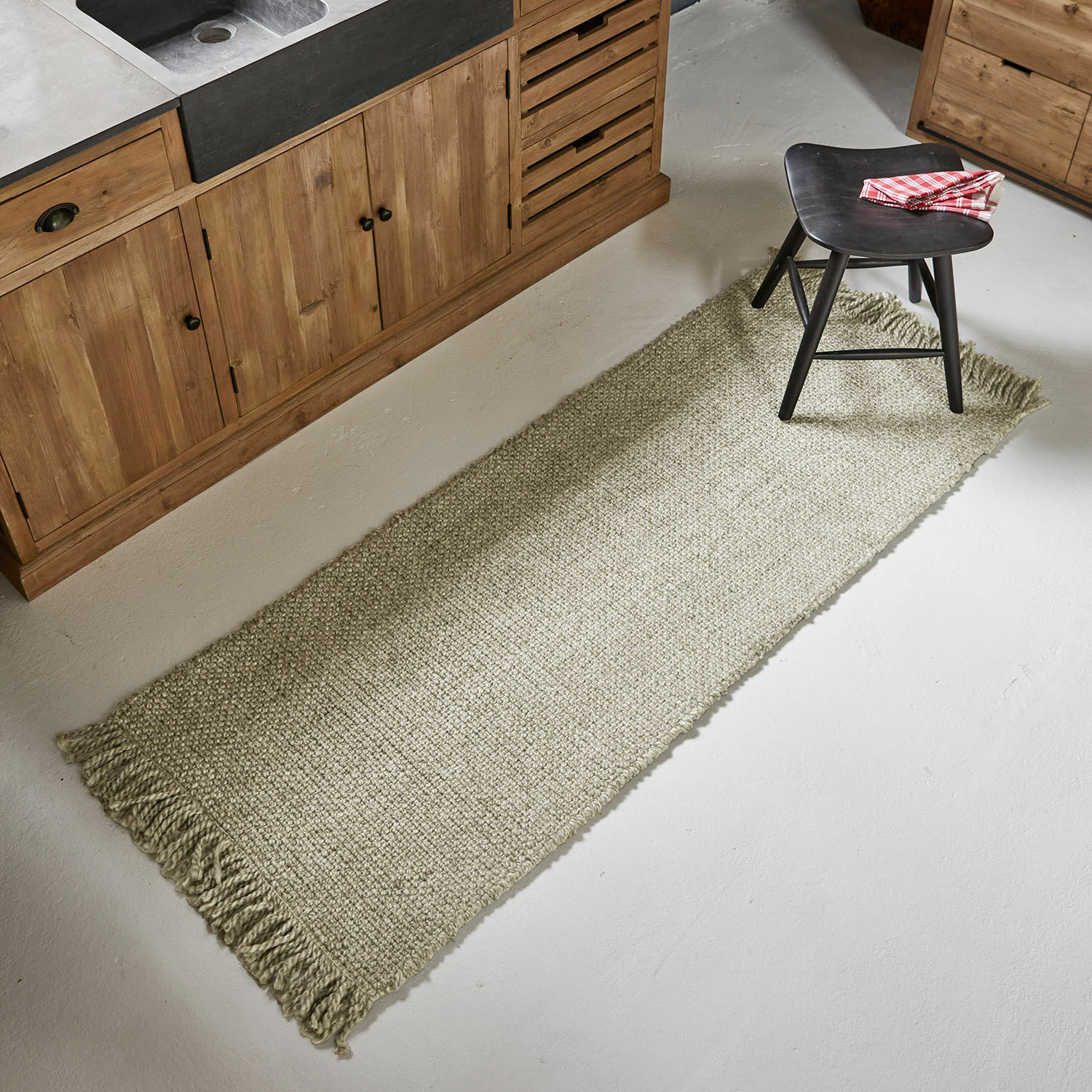 Beiger Teppichläufer mit Fransen aus Naturmaterial vor Holzküchenschränken auf hellem Boden