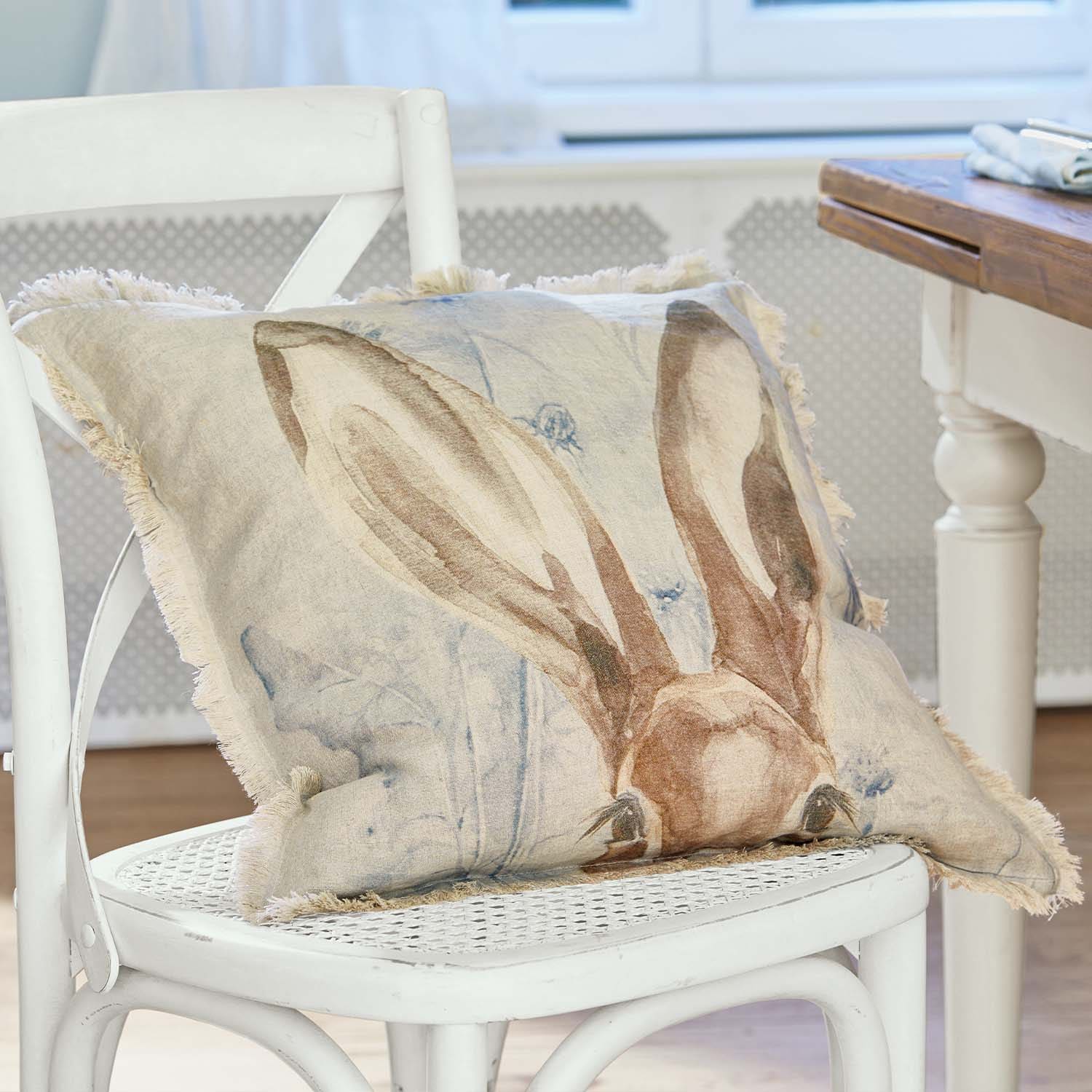 Beige Leinenkissen mit Hasenohren-Motiv und Fransen auf weißem Stuhl im Wohnzimmer