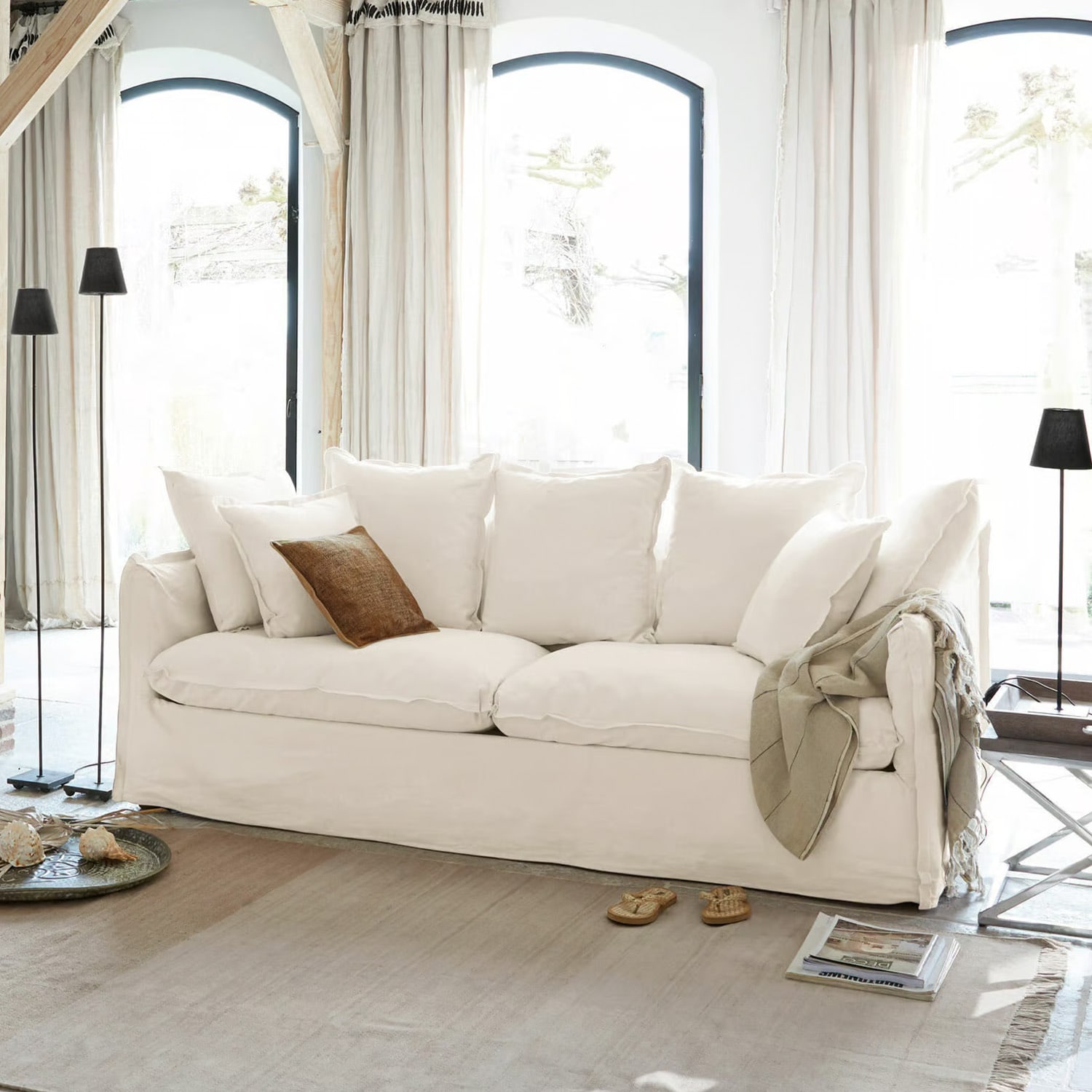 Großes weißes Baumwollsofa mit Kissen und braunem Dekokissen in hellem Wohnzimmer