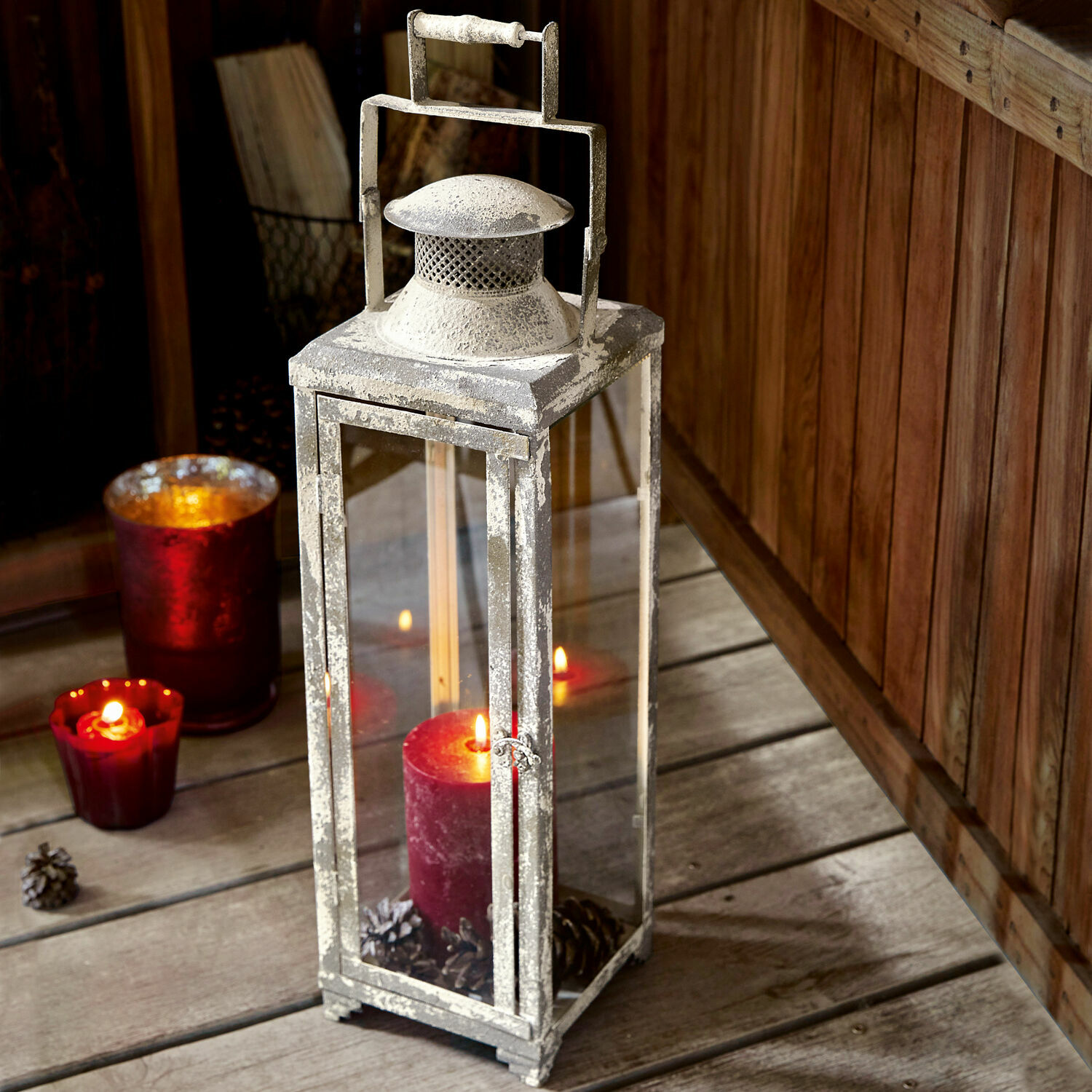 Laterne Isodore Metalllaterne im Vintage-Stil mit weißer Patina und roter Kerze auf Holzboden