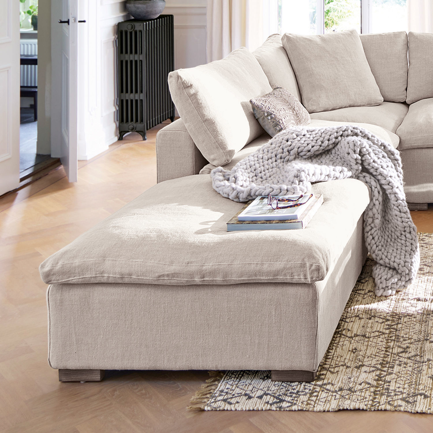 Hocker Bennington Beige Ecksofa aus Stoff mit weicher Decke und Kissen in hellem Wohnzimmer mit Holzboden