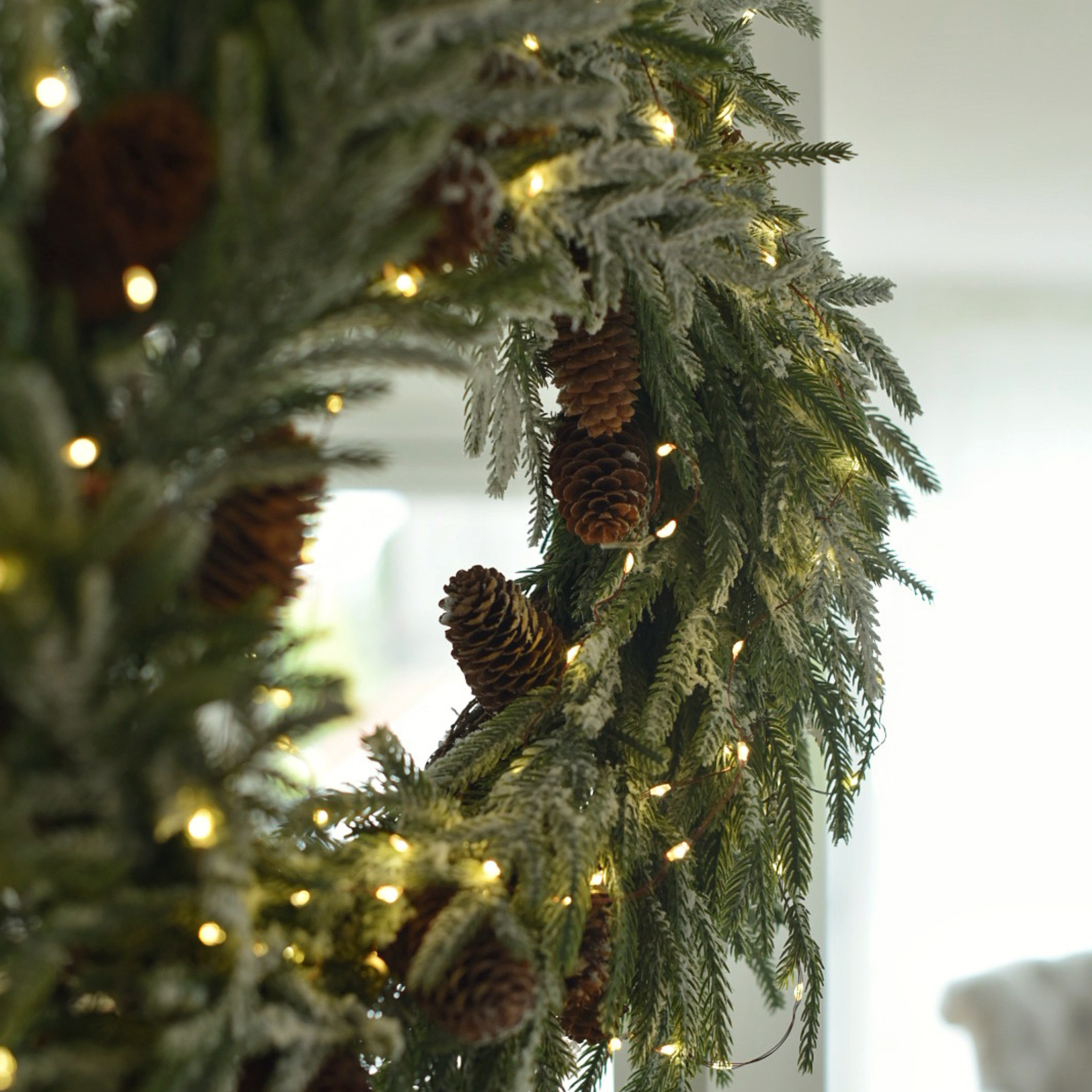 Weihnachtskranz aus grünen Zweigen mit Zapfen und warmweißer LED-Lichterkette als Winterdekoration