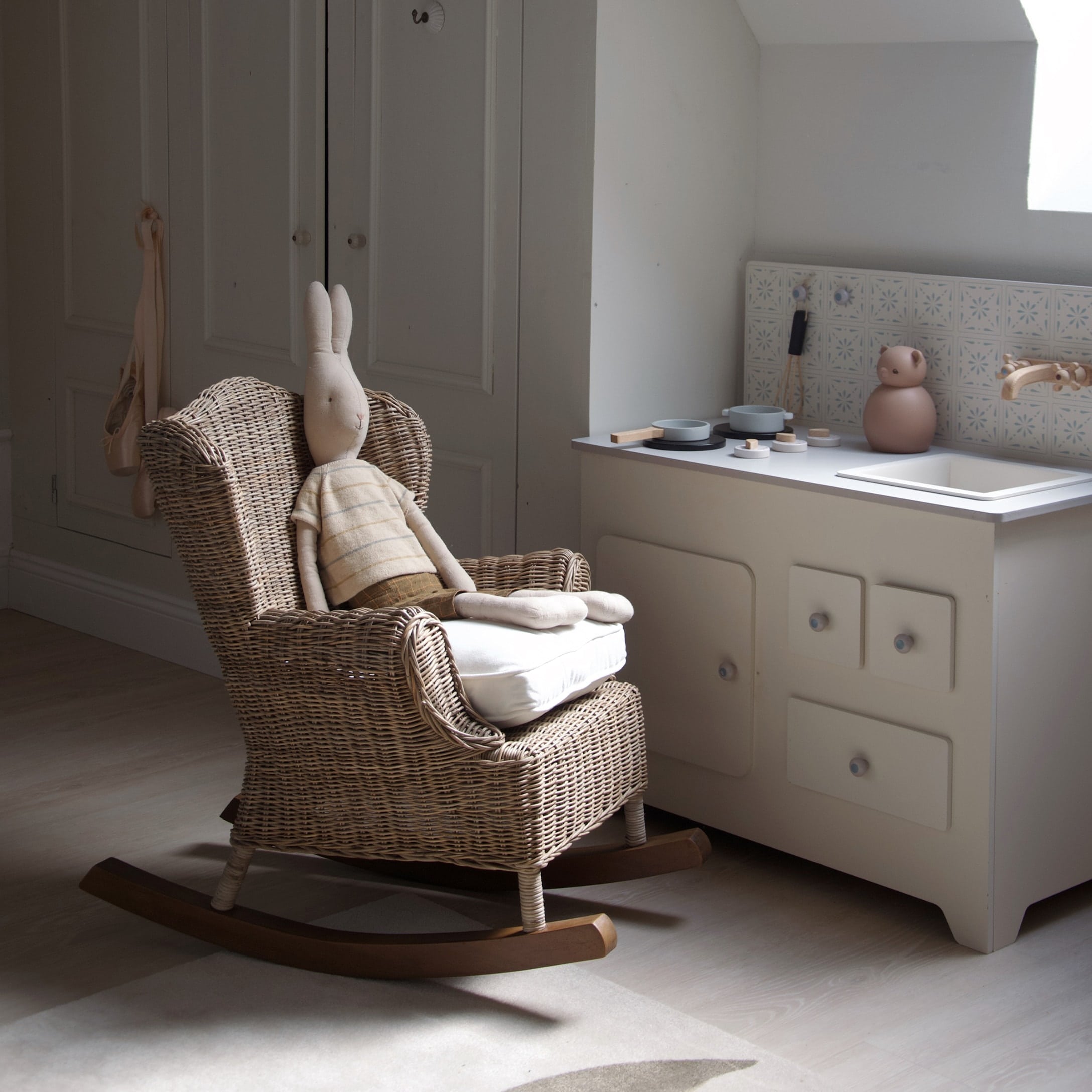Kinderzimmer mit Rattanschaukelstuhl und heller Spielküche in natürlichen Farbtönen