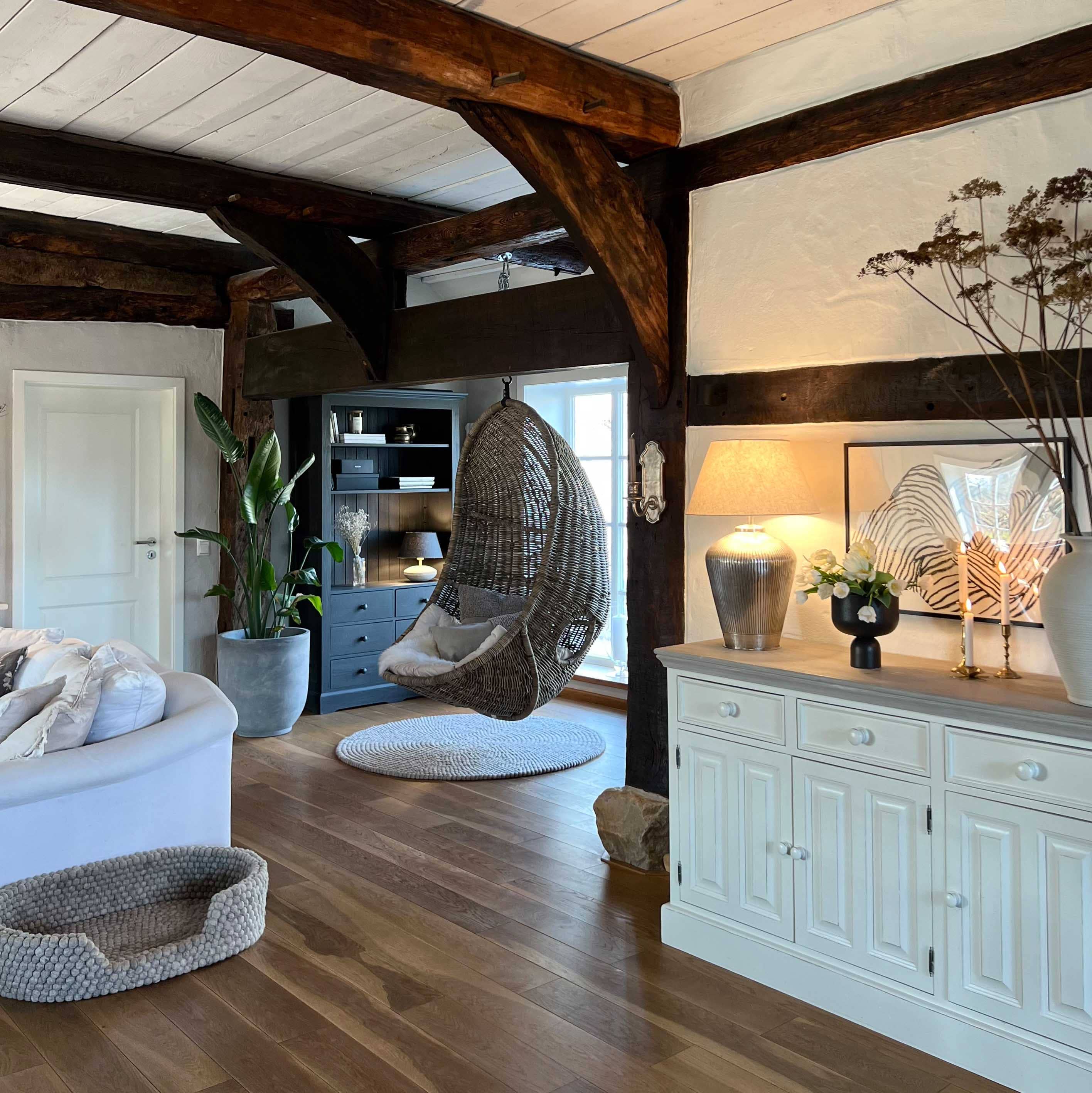 Hängesessel aus grauem Rattan in gemütlichem Wohnzimmer mit Holzboden und weißem Sideboard