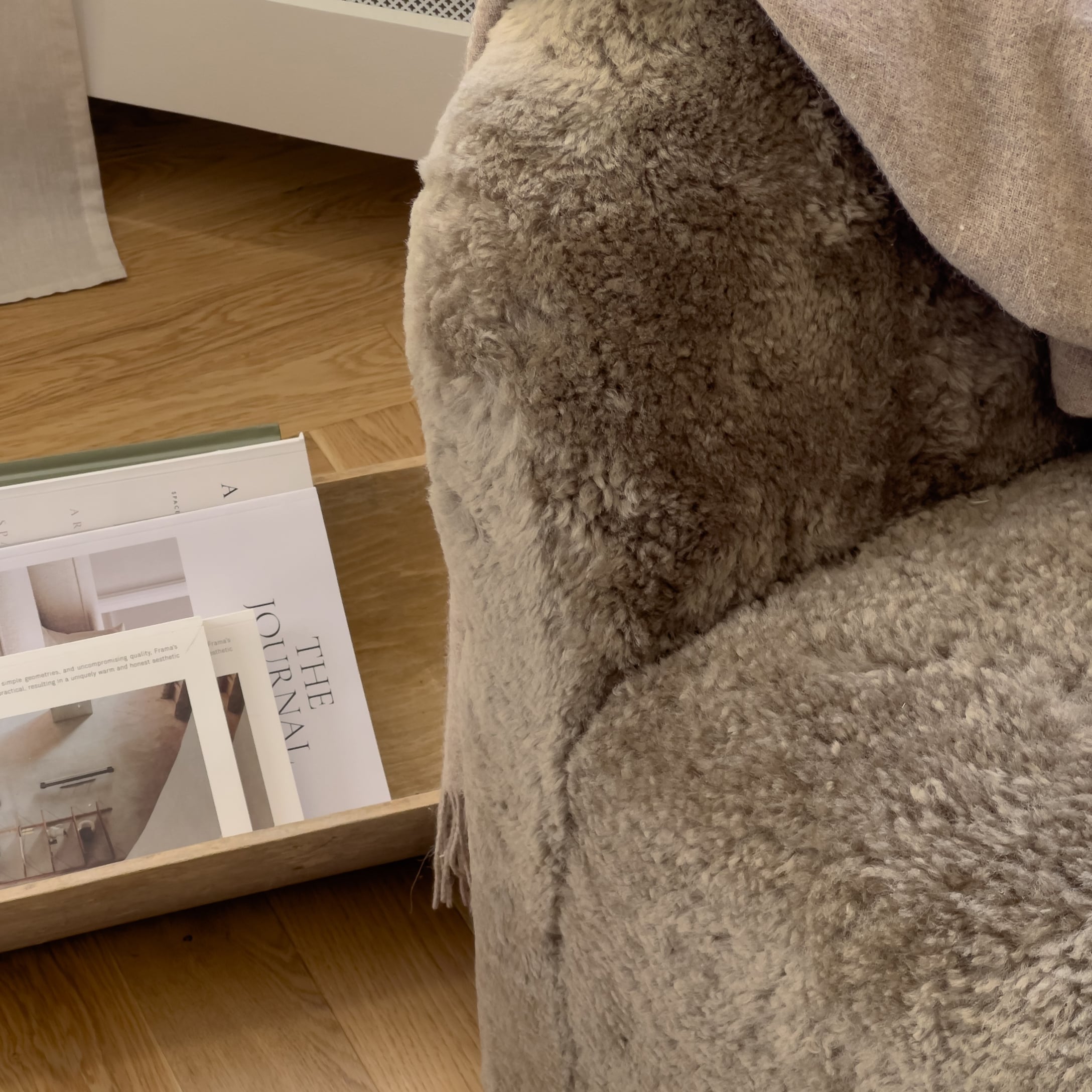 Weicher beiger Fell-Kuscheldecke auf Sessel neben Holztablett mit Zeitschriften, gemütliches Wohnaccessoire