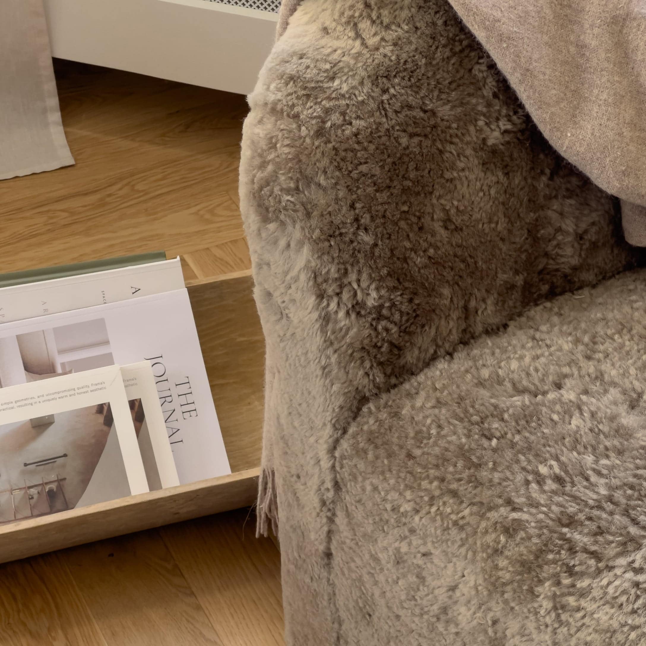 Weicher beiger Fell-Kuscheldecke auf Sessel neben Holztablett mit Zeitschriften, gemütliches Wohnaccessoire