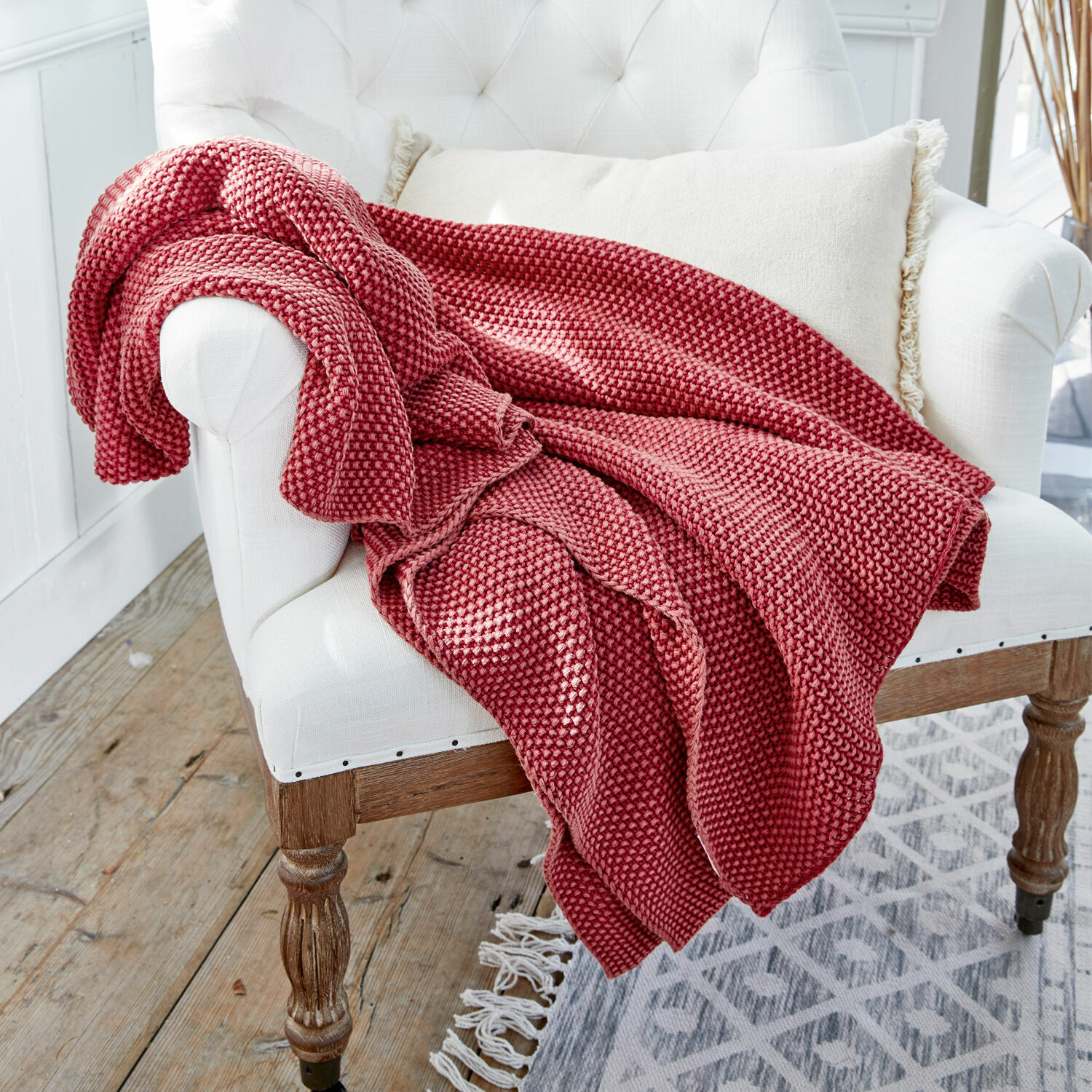 Plaid Amberley Roter gestrickter Kuscheldecke aus weichem Material auf weißem Sessel in hellem Raum