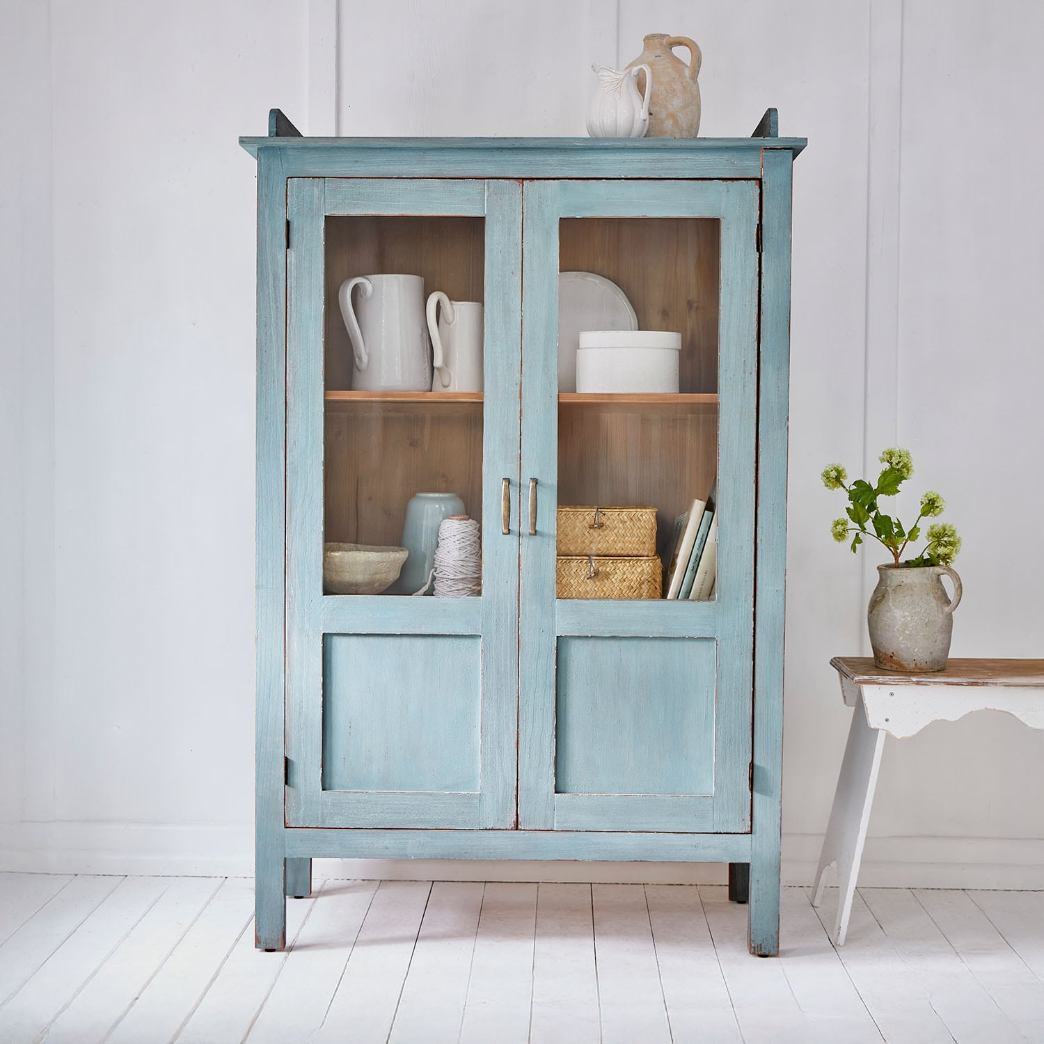 Blauer Holzschrank mit Glastüren und Vintage-Keramikdekoration in hellem Raum