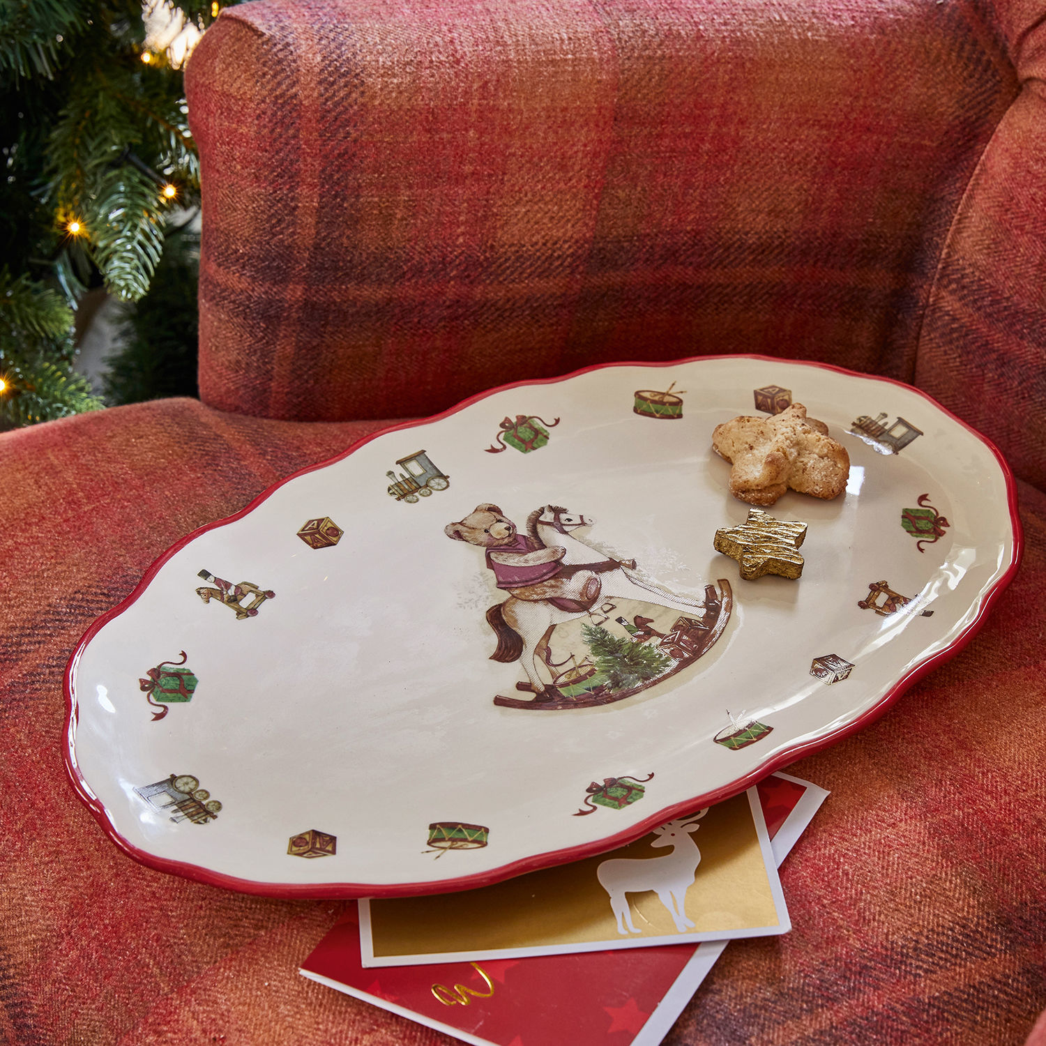 Platte Troms Keramikteller mit Weihnachtsmotiv Bär auf Schaukelpferd und rotem Rand auf rotem Sofa